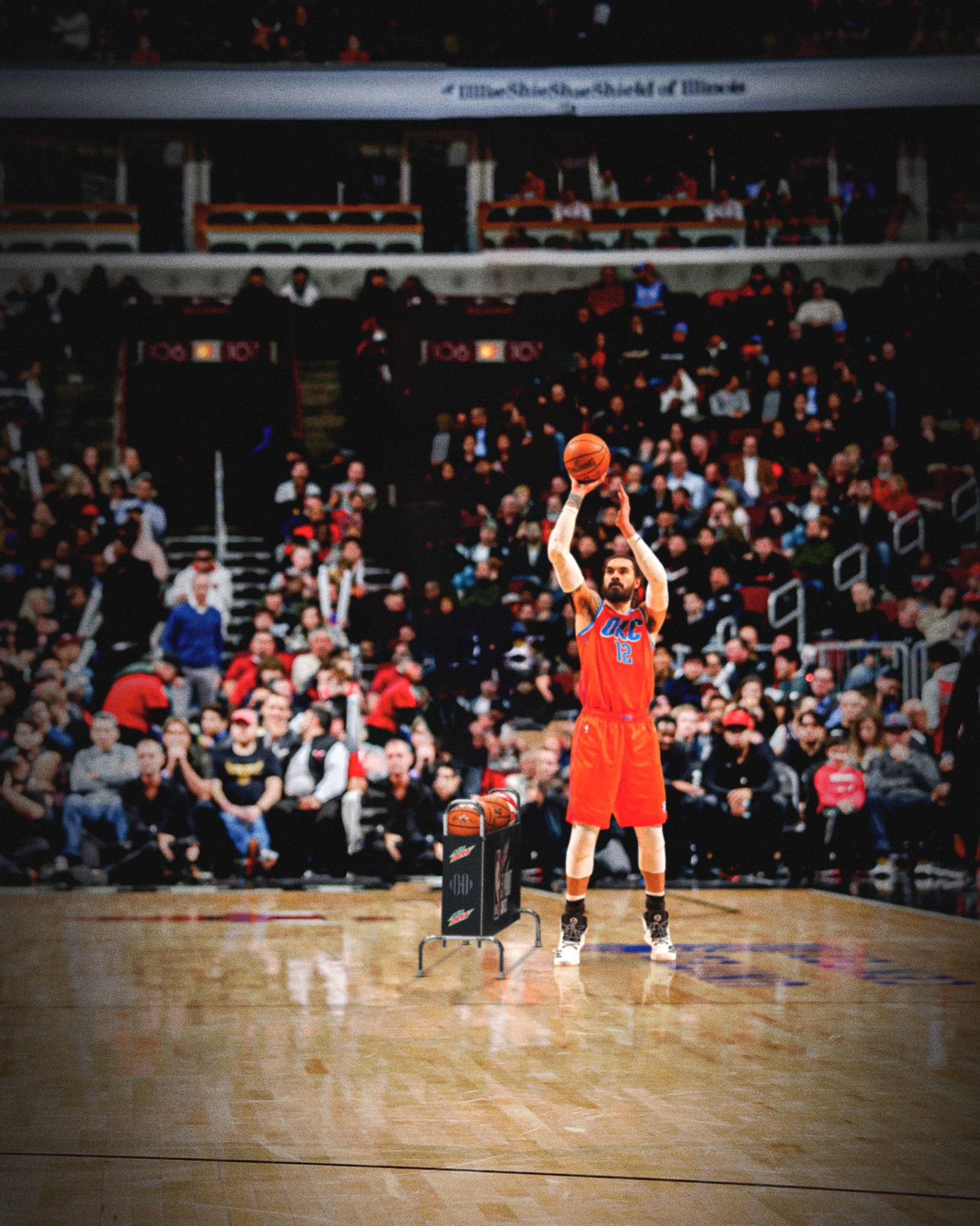 Steven Adams 桌布 壁紙 — 一名身穿橙色球衣的籃球運動員在明亮的場館燈光下，在全場觀眾專注注視中，投出一個罰球。
