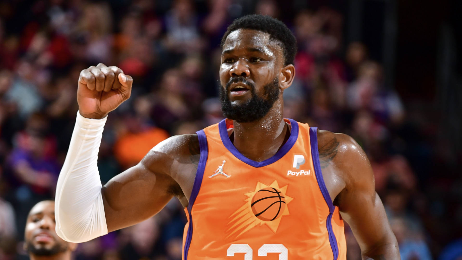 NBA 桌布 壁紙 — 一名身穿橙色球衣的籃球運動員在比賽中高舉拳頭慶祝勝利，身後是模糊的人群。