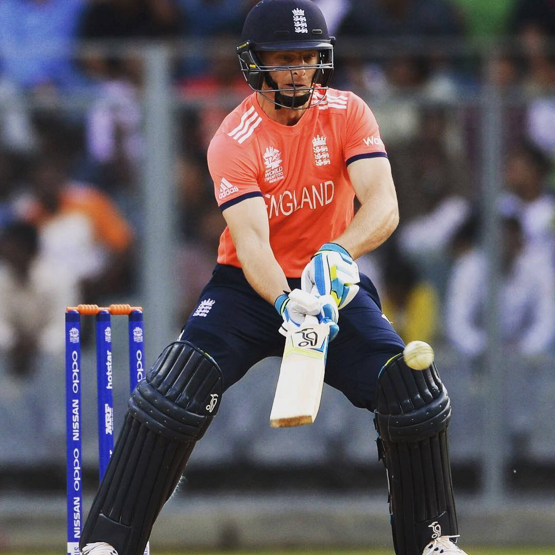 England Cricket 桌布 壁紙 — 一名身穿橙色球衣的英格蘭板球運動員在日間比賽中，背景有觀眾，揮動球棒擊打來球。