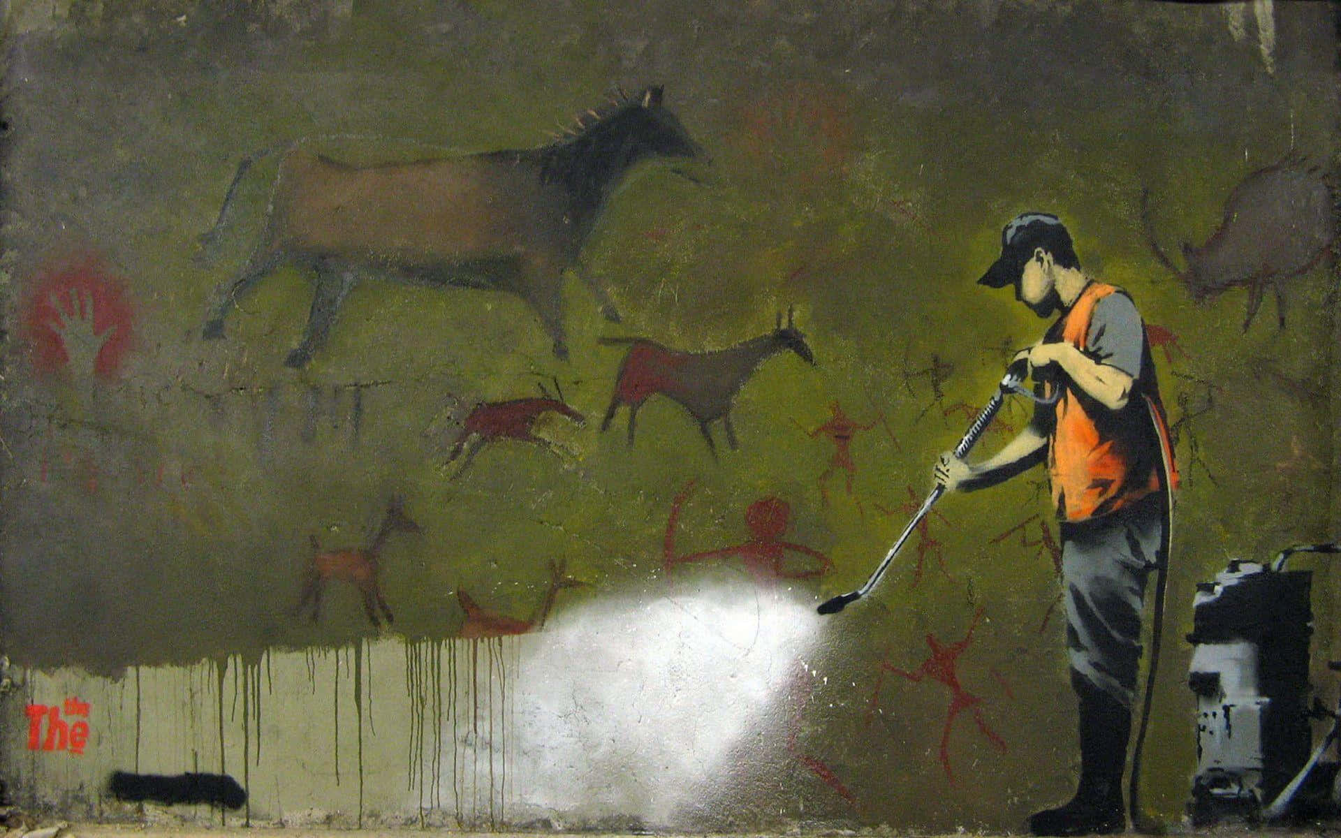 Banksy 桌布 壁紙 — 一名身穿橙色背心的工人使用高壓水槍清除牆上的古代洞穴壁畫，露出下面的裸露混凝土。