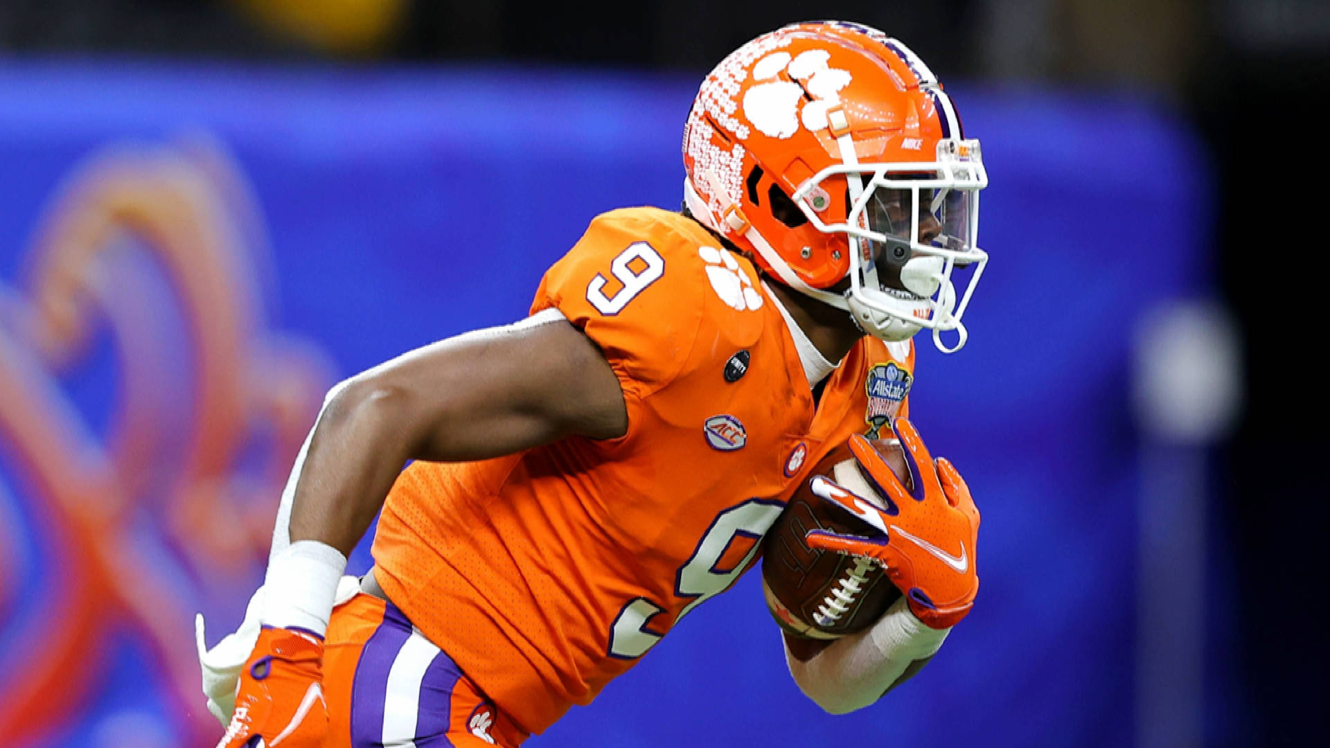 Travis Etienne 桌布 壁紙 — 一名身穿橙色裝備的克萊姆森足球員在體育場燈光下的夜間比賽中帶球衝刺。
