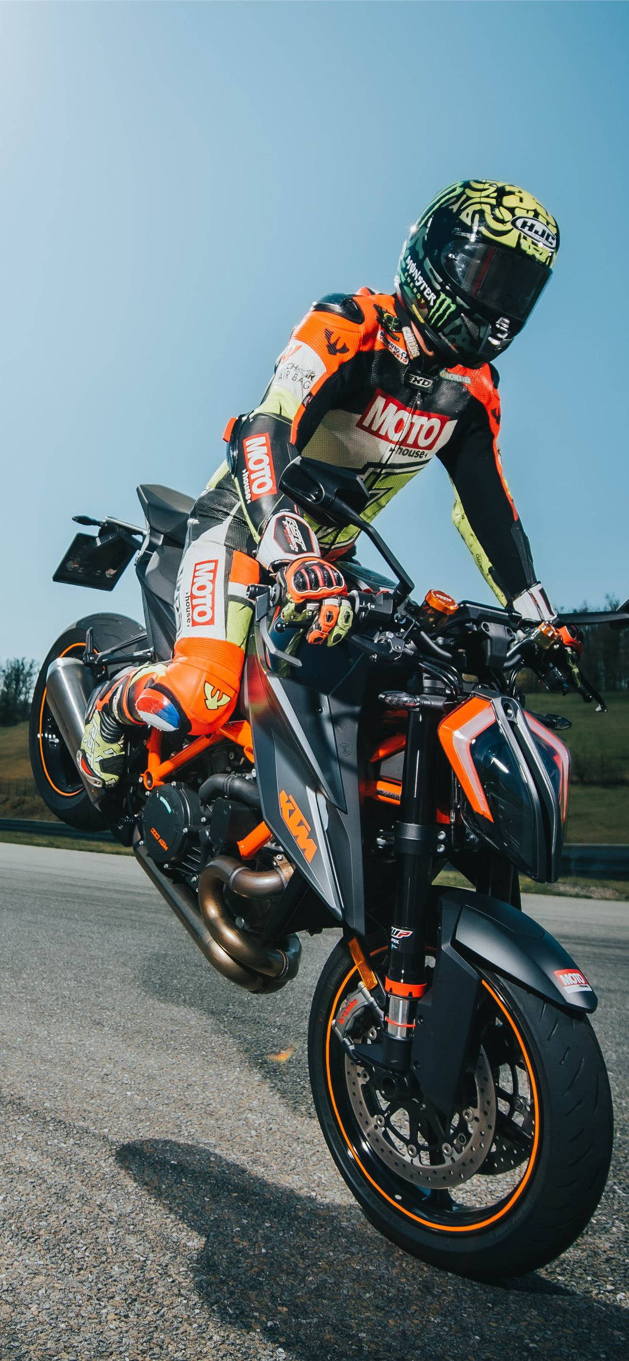 KTM RC 200 桌布 壁紙 — 一名身穿橙色裝備的摩托車手在晴朗的藍天下，駕駛跑車摩托車表演前輪離地。