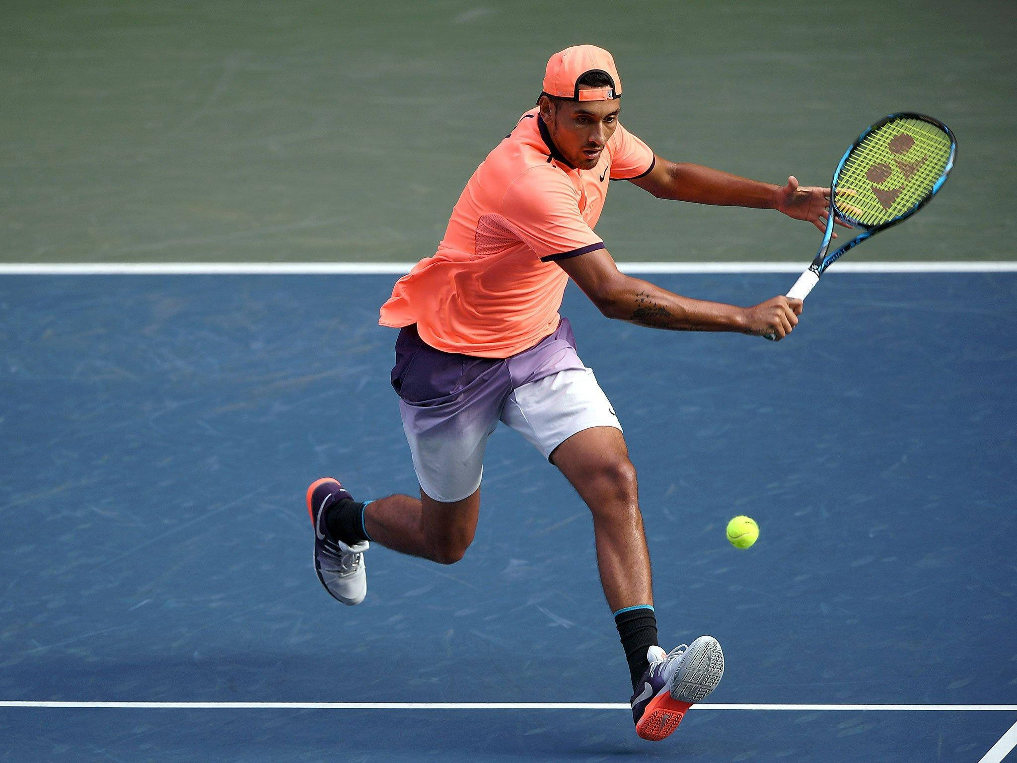 Kyrgios 桌布 壁紙 — 一名身穿橙色襯衫和帽子的男性網球運動員在藍色球場上向前撲身，用球拍擊打黃色球。