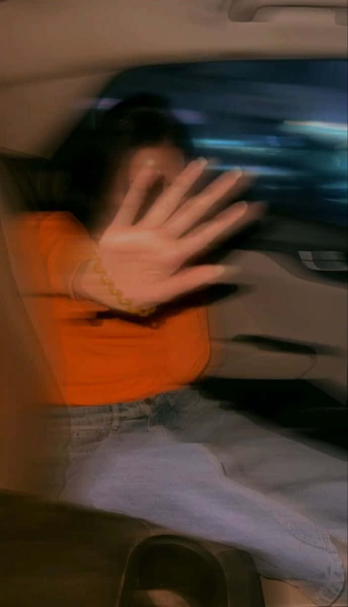 waving 桌布 壁紙 — 一名身穿橙色襯衫的人在夜間從行駛中的汽車揮手，模糊的城市燈光掠過。