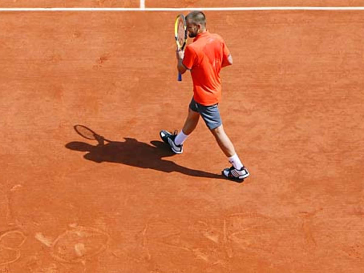 Tennis 桌布 壁紙 — 一名身穿橙色襯衫的男網球選手在陽光明媚的紅土球場上拿著球拍走過。