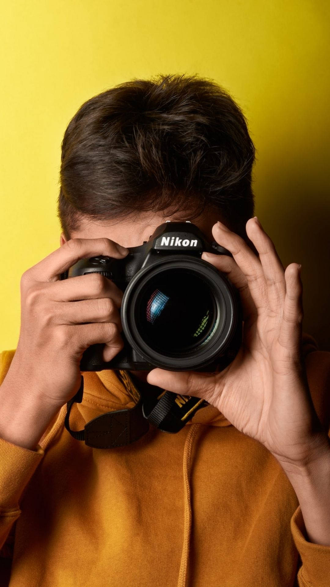身穿橙色連帽衫的人將Nikon DSLR相機舉在臉前。