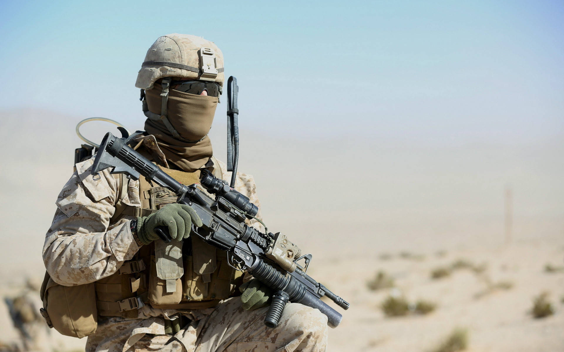 Marine Corps 桌布 壁紙 — 一名身穿沙漠迷彩的士兵在明亮的日光下，跪著持步槍，背景是朦朧乾旱的景觀。
