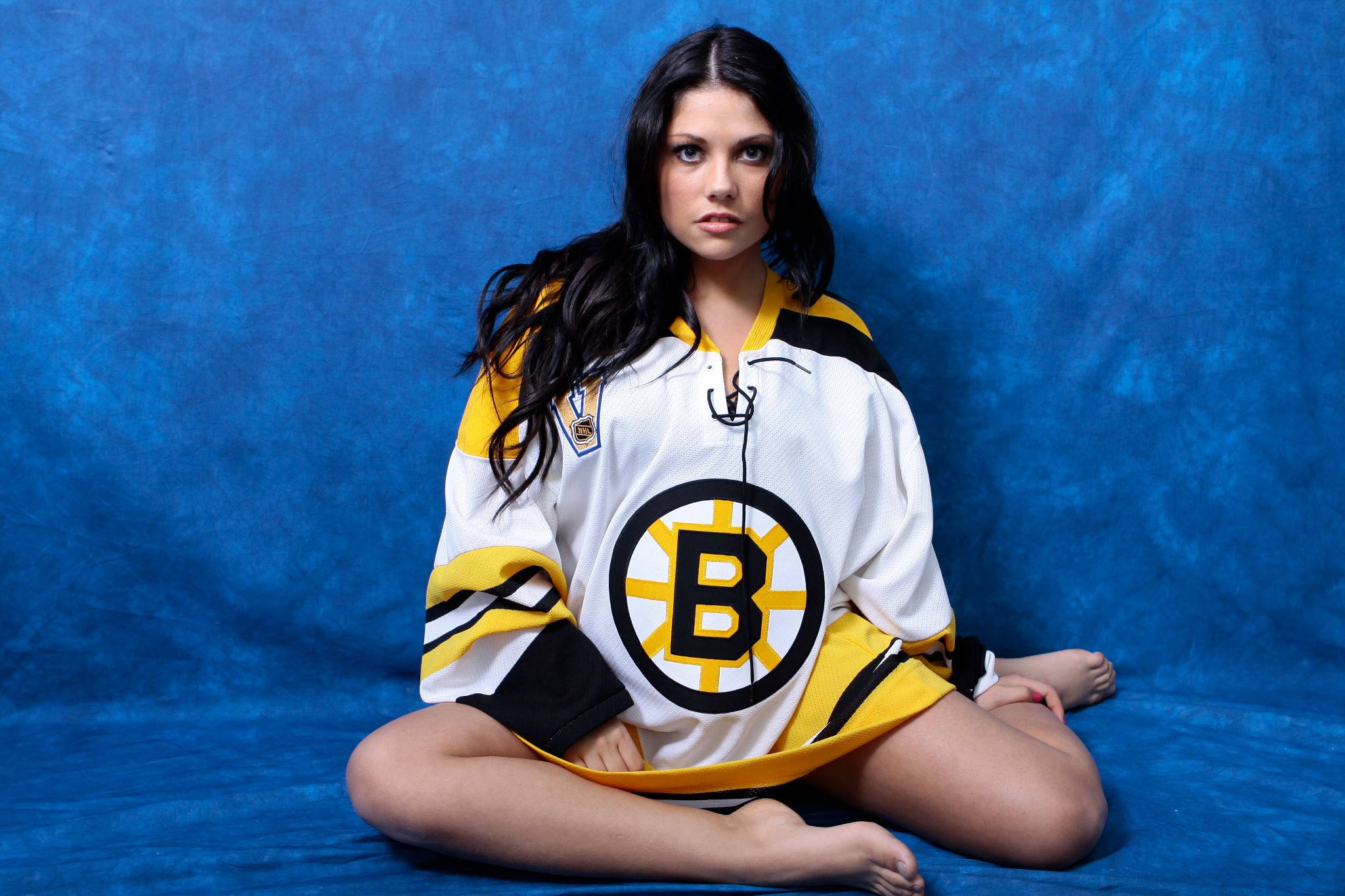 bruins 桌布 壁紙 — 一名身穿波士頓棕熊隊冰球球衣的女性，在帶有紋理的藍色背景上盤腿而坐，眼神專注。