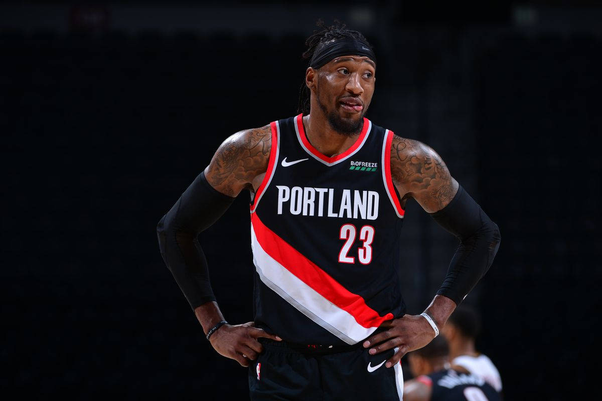 robert covington 桌布 壁紙 — 一名身穿波特蘭拓荒者球衣的籃球運動員，雙手叉腰，站在黑暗的球場背景下。