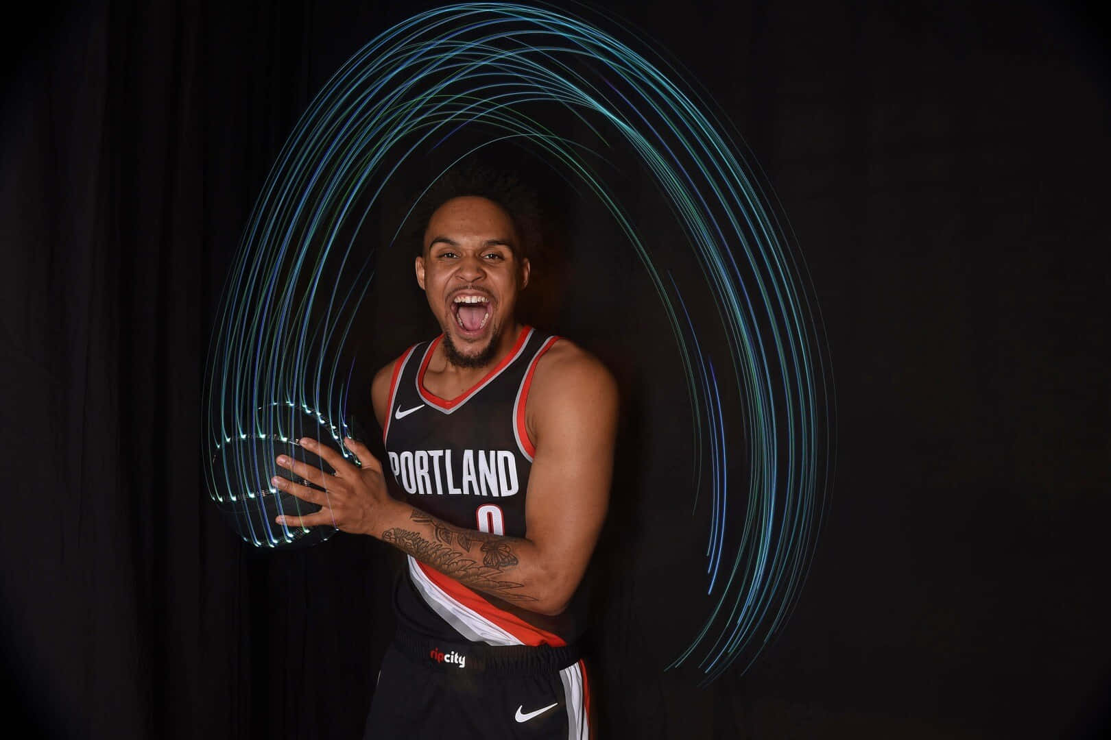 NBA 桌布 壁紙 — 一名身穿波特蘭球衣的籃球運動員在黑色背景下咆哮，散發能量，發光的藍色光軌在他周圍旋轉。