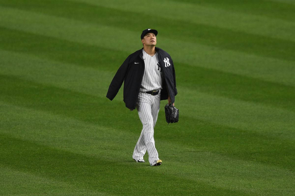 masahiro tanaka 桌布 壁紙 — 一名身穿洋基隊球衣的棒球運動員在球場燈光下走過一條精心條紋的綠色場地。