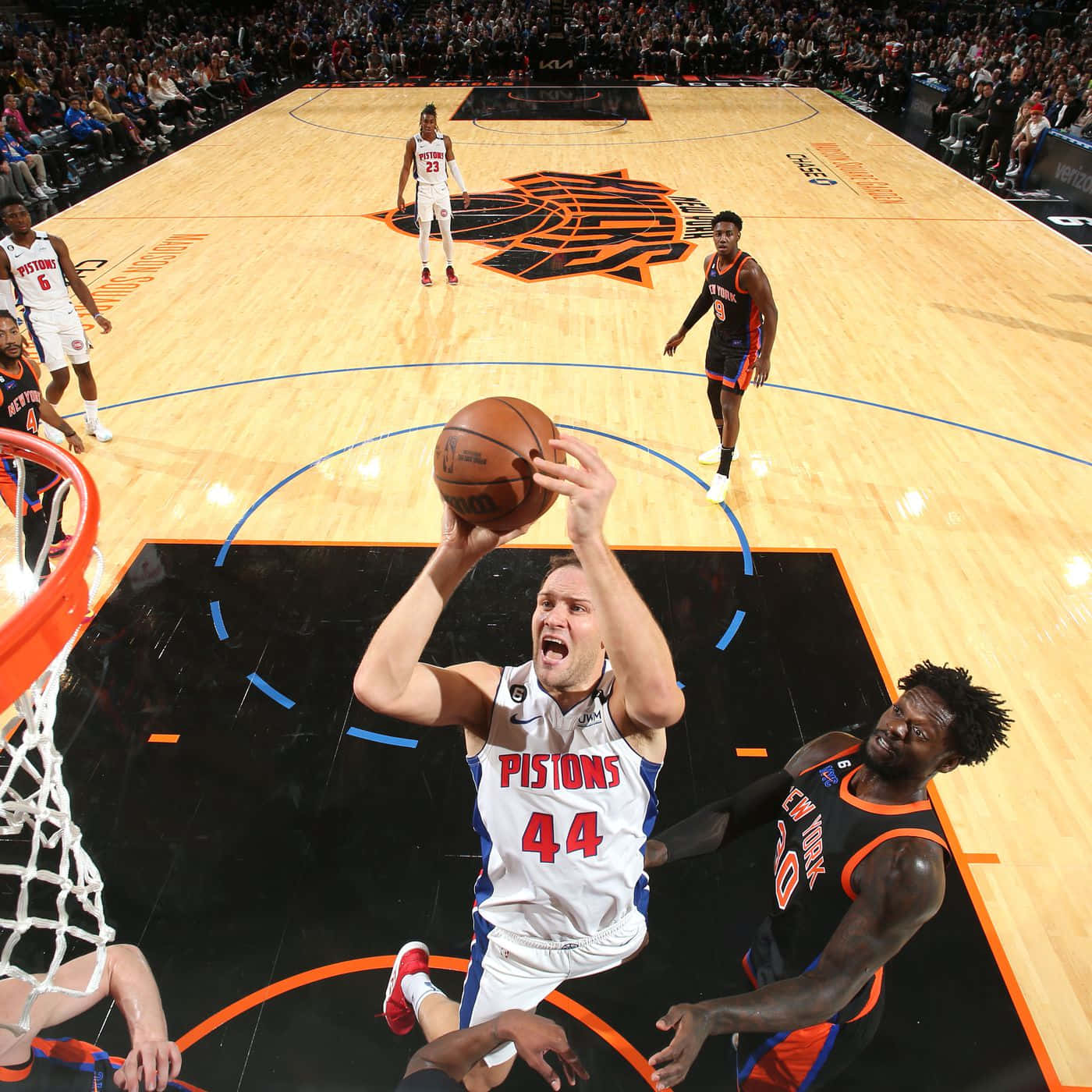 NBA 桌布 壁紙 — 一名身穿活塞隊球衣的籃球運動員在明亮的場館燈光下灌籃，防守球員跳起試圖封阻。