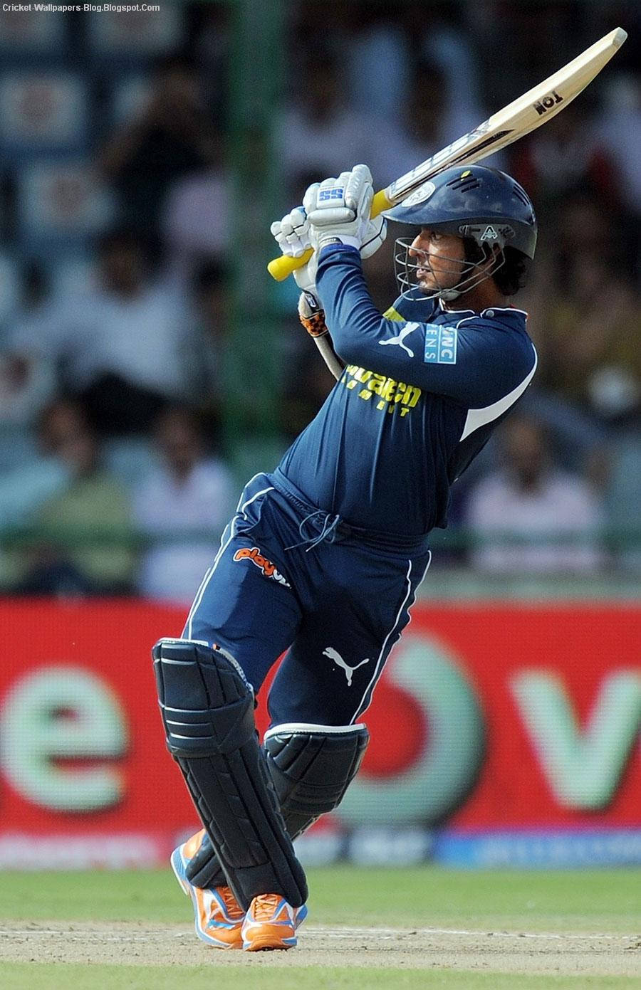 Sri Lanka Cricket 桌布 壁紙 — 一名身穿海軍藍制服的板球擊球手在綠色場地上揮動球棒，背景有模糊的觀眾。
