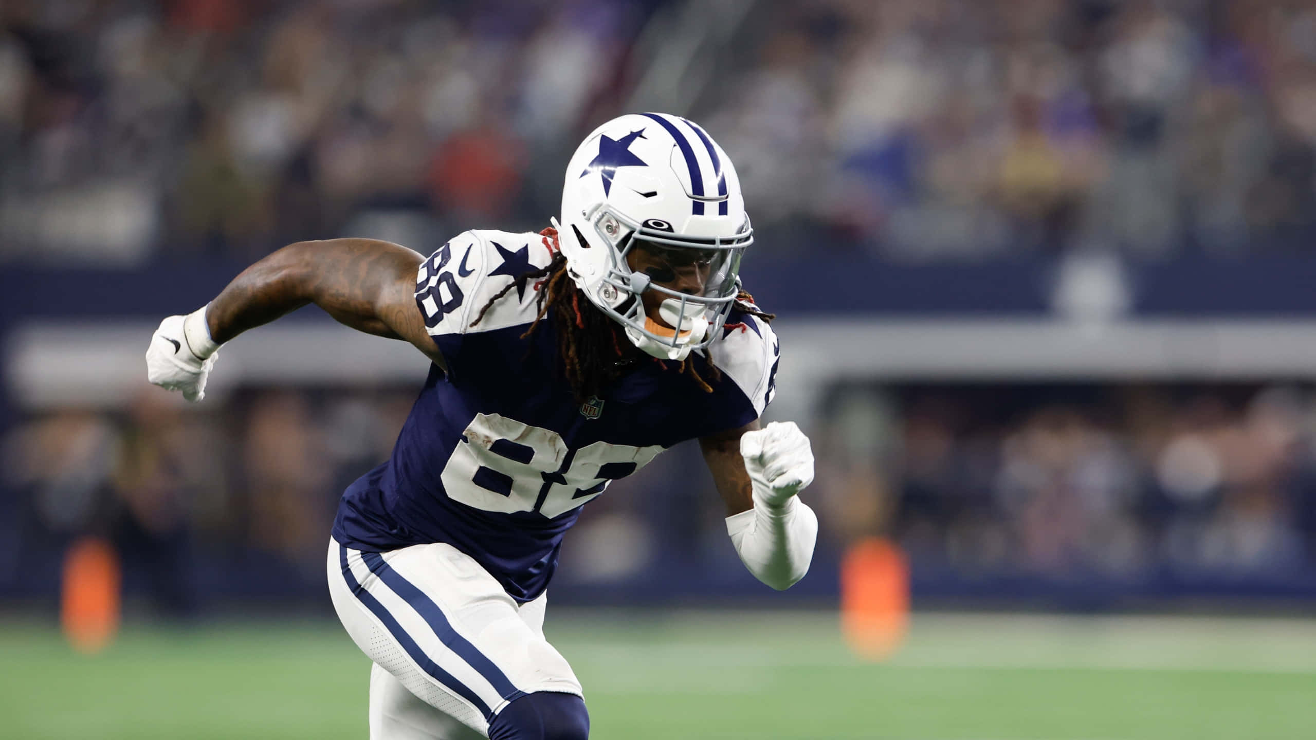 Dallas Cowboys Players 桌布 壁紙 — 一名身穿海軍藍和白色球衣的達拉斯牛仔隊美式足球員在球場燈光下動態地衝刺。