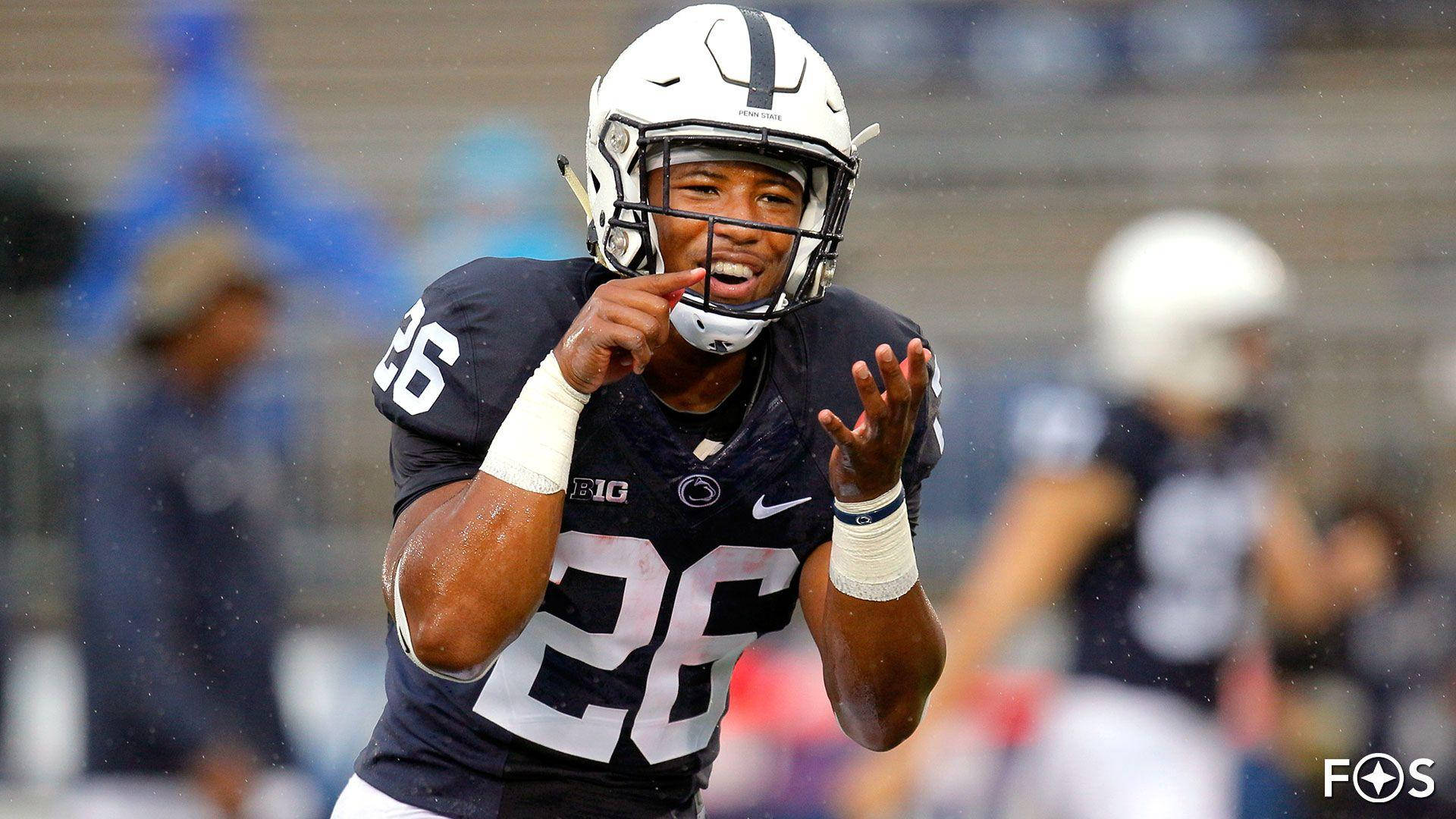 Saquon Barkley 桌布 壁紙 — 一名身穿海軍藍球衣、號碼26的美式足球員在雨中的球場上高舉雙手，面露喜悅地慶祝。