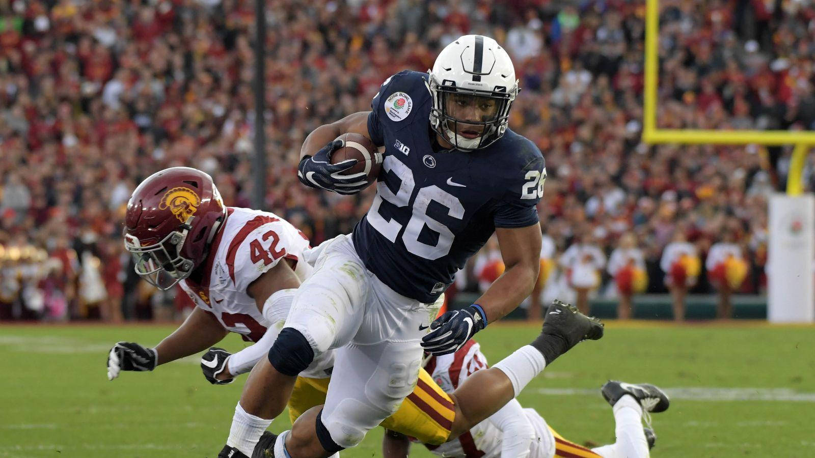 Saquon Barkley 桌布 壁紙 — 一名身穿海軍藍球衣26號的賓州州立大學美式足球員，在持球衝刺時被一名身穿紅金色的南加州大學防守球員擒抱。