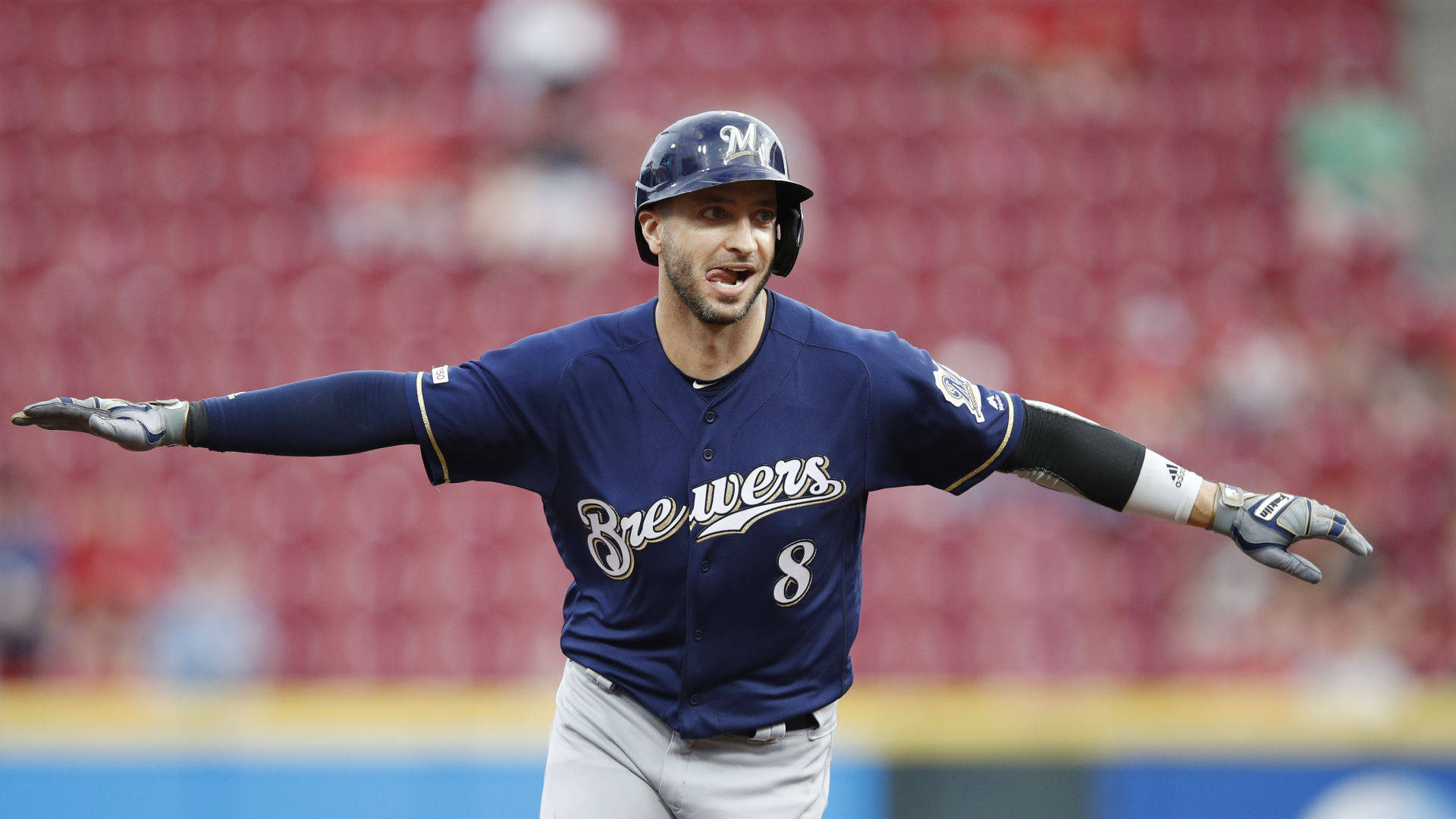 Brewers 桌布 壁紙 — 一名身穿海軍藍球衣的密爾瓦基釀酒人棒球手在陽光明媚的球場上張開雙臂慶祝。