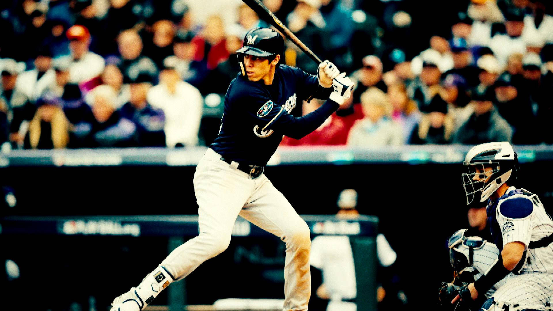 Brewers 桌布 壁紙 — 一名身穿海軍藍球衣的棒球打擊手在擠滿觀眾的球場上強力揮棒，捕手蹲在他身後。