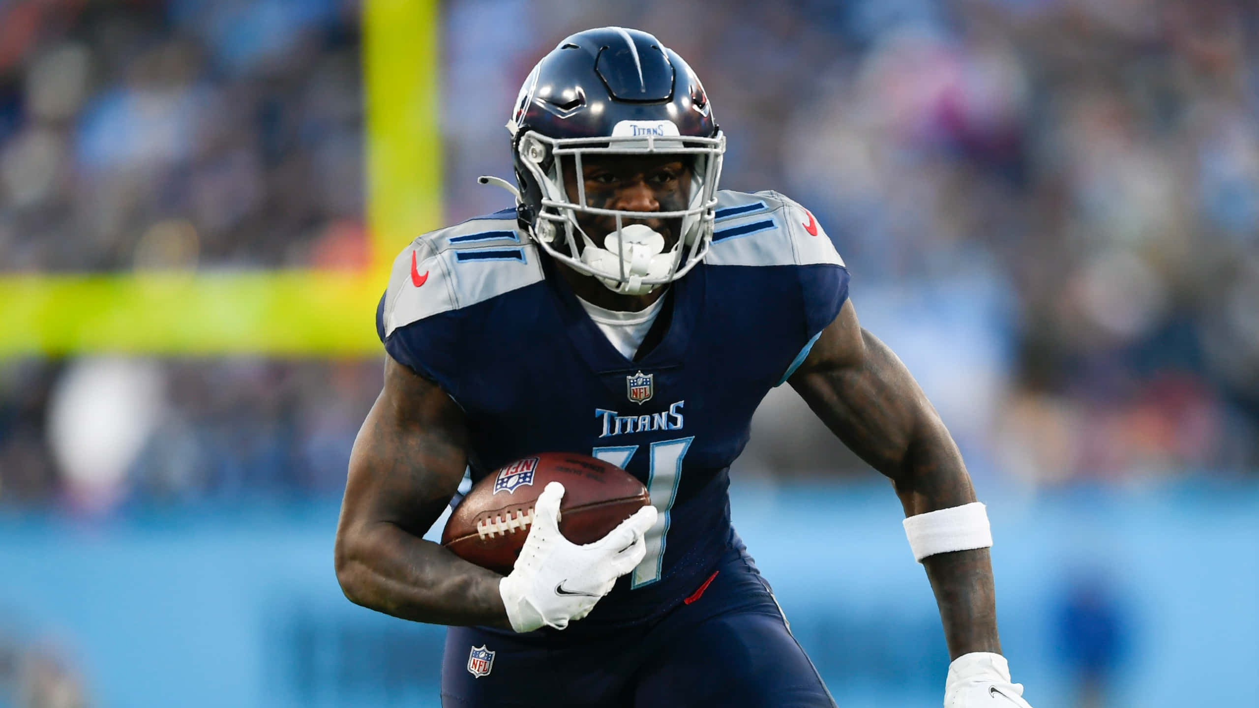 American 桌布 壁紙 — 一名身穿海軍藍球衣的田納西泰坦隊美式足球員在球場燈光下比賽中持球衝刺。