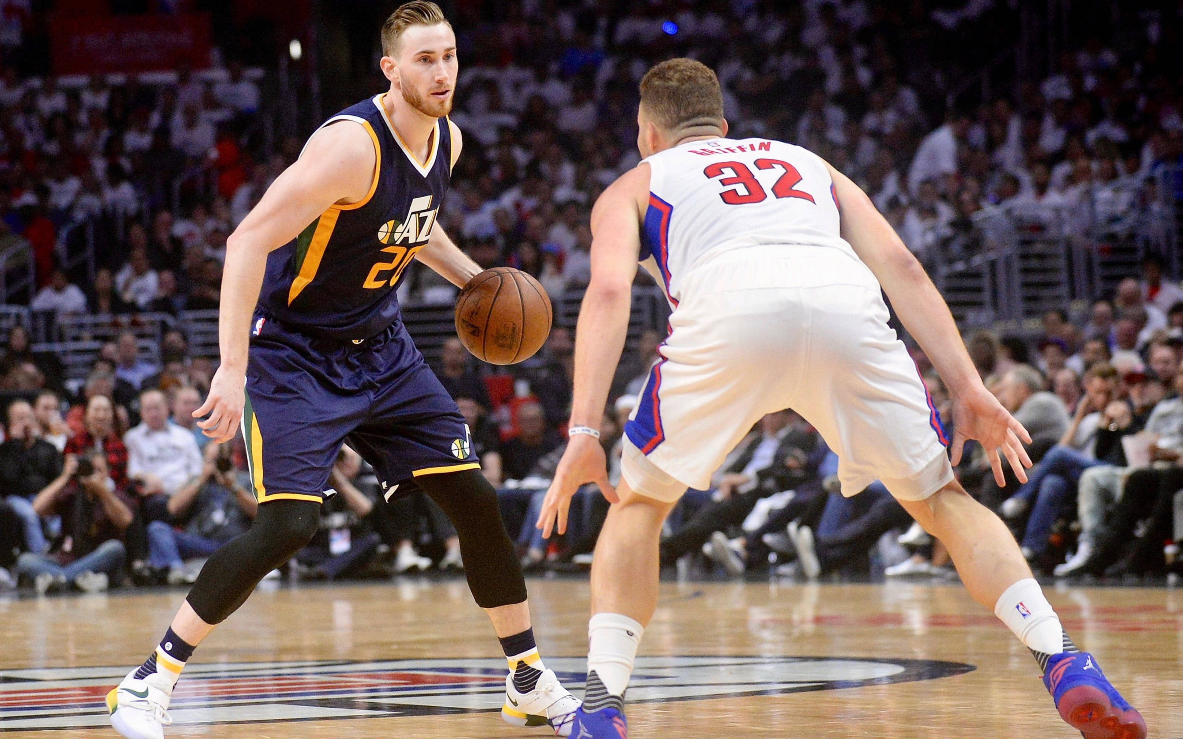 gordon hayward 桌布 壁紙 — 一名身穿海軍藍球衣的籃球運動員在現場比賽中運球，同時被一名身穿白色球衣的對手防守。