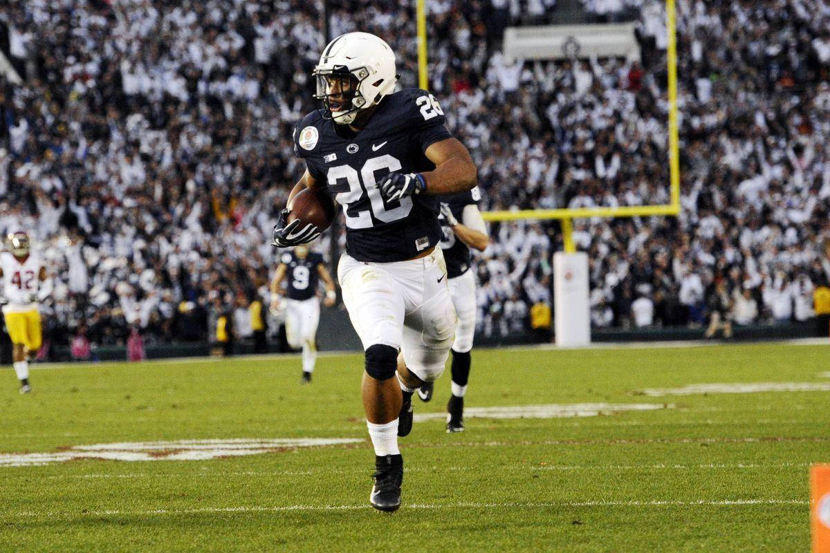 Saquon Barkley 桌布 壁紙 — 一名身穿海軍藍球衣的足球員帶著球在場上衝刺，而座無虛席的球場在球場燈光下觀看。