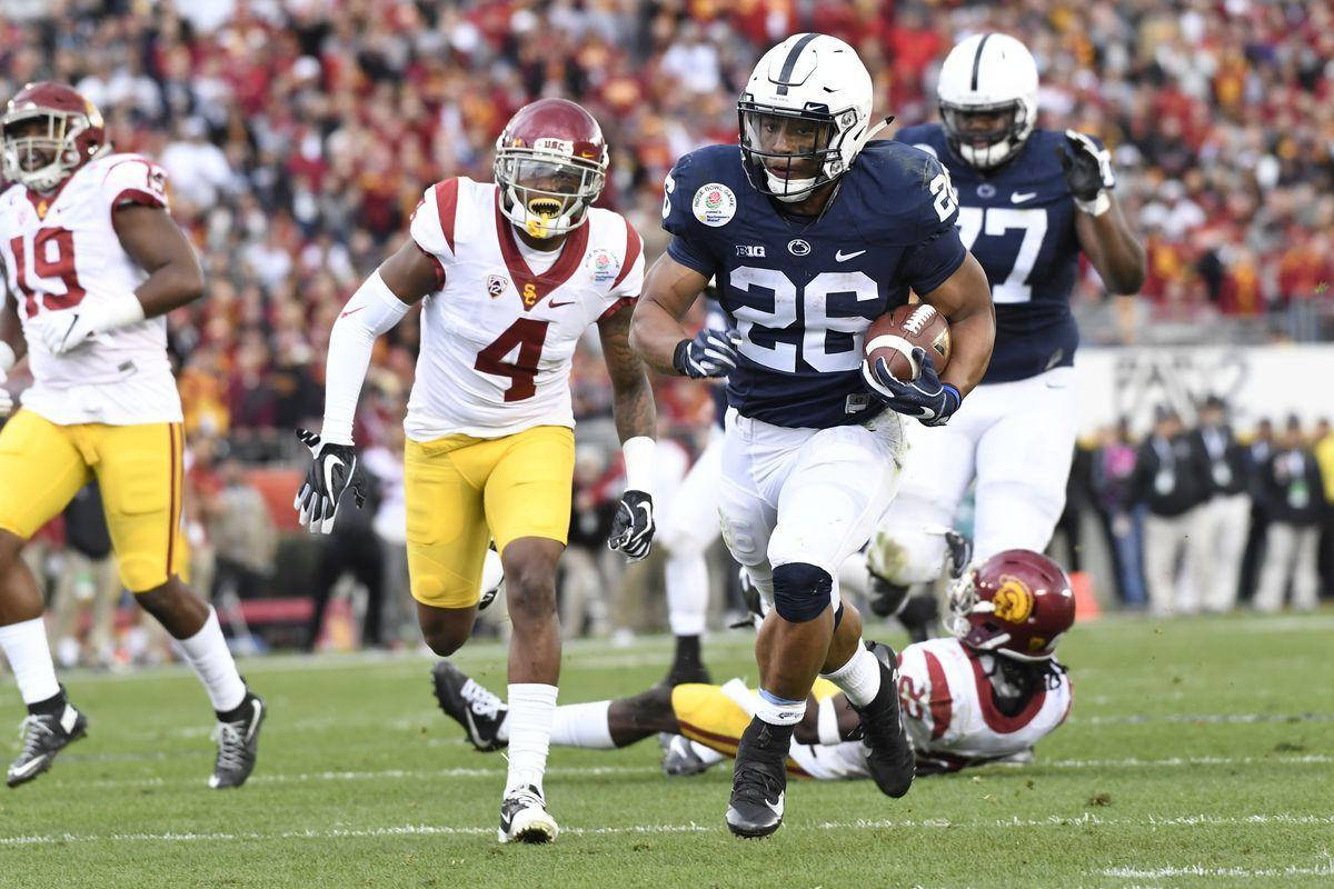 Saquon Barkley 桌布 壁紙 — 一名身穿海軍藍球衣的足球運動員在充滿活力的綠色球場上帶球奔跑，對手在後面追趕。