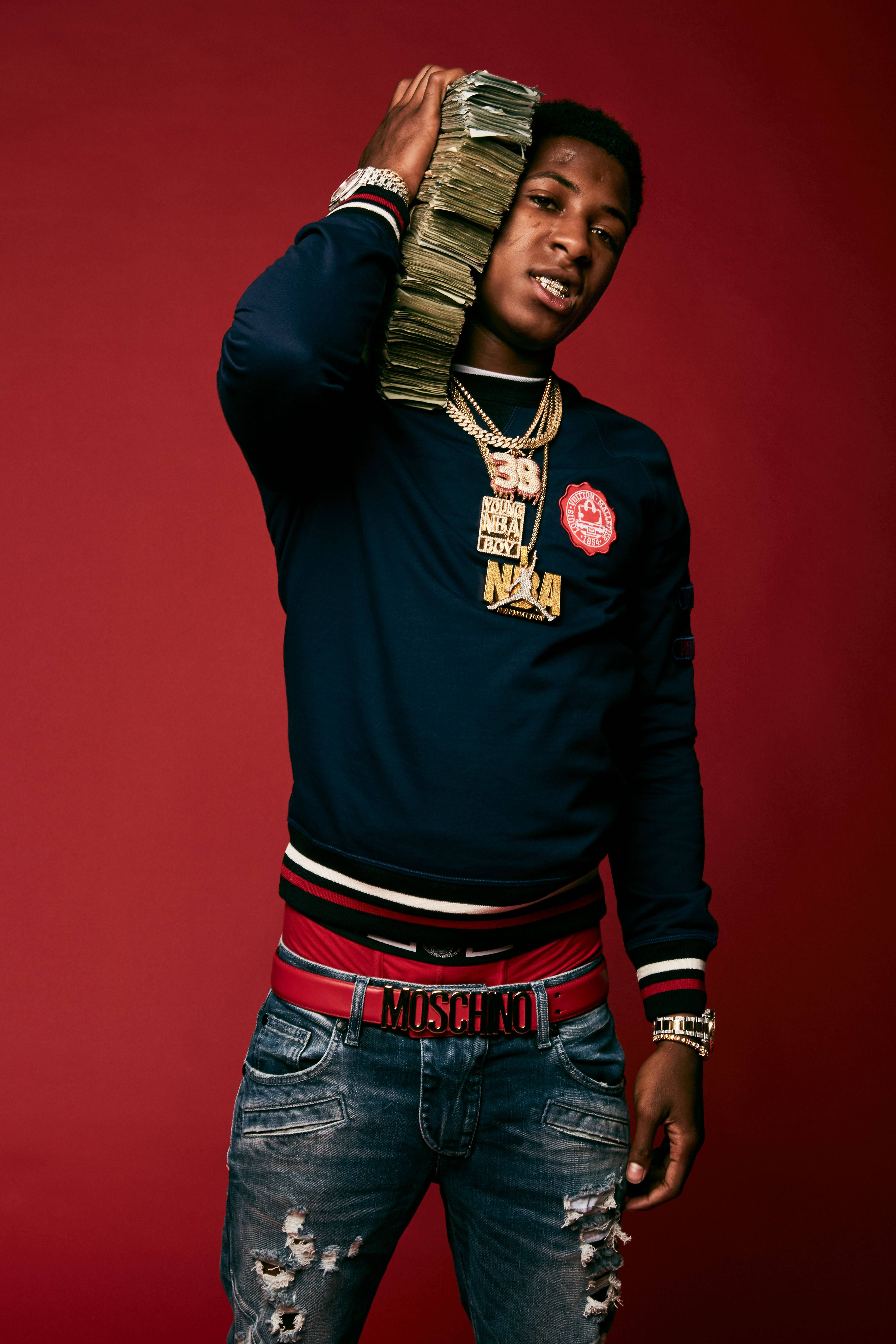 Youngboy 桌布 壁紙 — 一名身穿海軍藍衛衣和破洞牛仔褲的年輕男子，在深紅色工作室背景前將一疊現金高舉過頭。