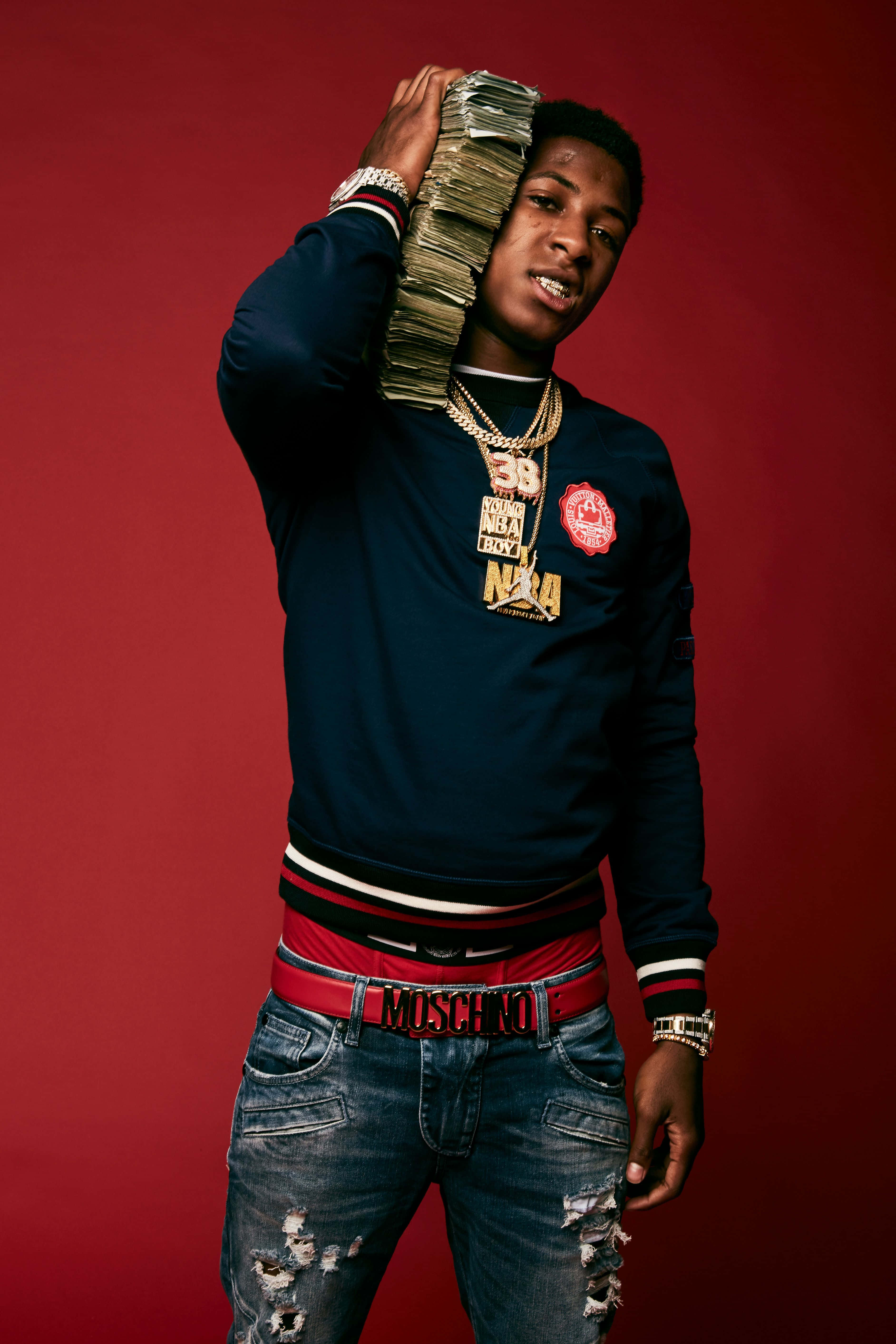 Youngboy 桌布 壁紙 — 一名身穿海軍藍衛衣和破洞牛仔褲的年輕男子，在深紅色背景前將一疊現金高舉過頭。