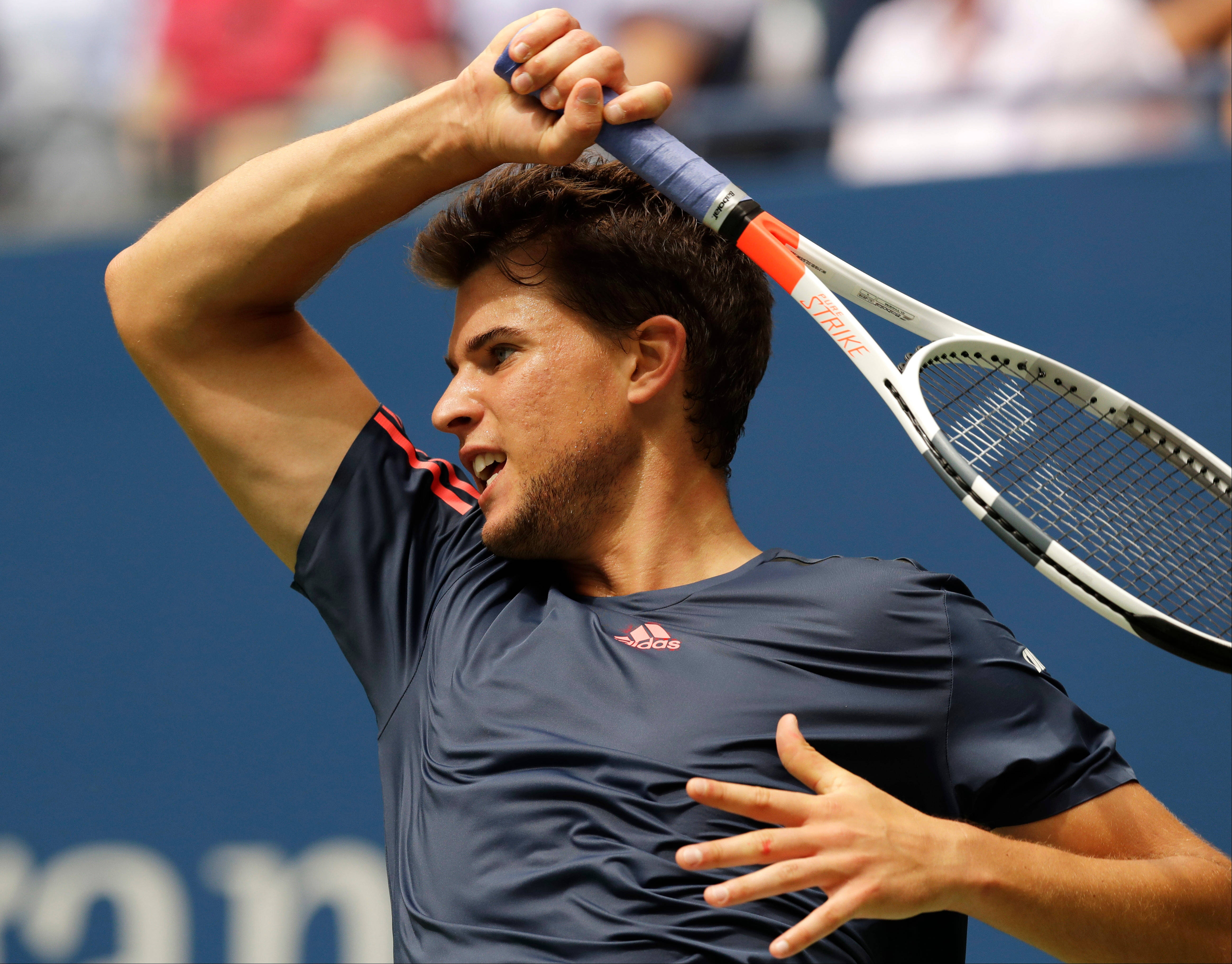 dominic thiem 桌布 壁紙 — 一名身穿海軍藍襯衫的男性網球選手在比賽中專注地將球拍握在頭頂上方。