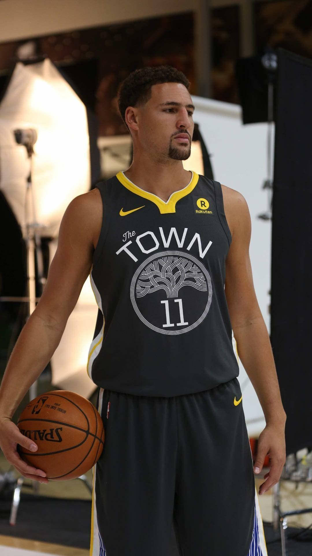 Thompson 桌布 壁紙 — 一名身穿深灰色「The Town」球衣的籃球運動員在柔光箱燈光照亮的攝影棚中手持Spalding籃球。