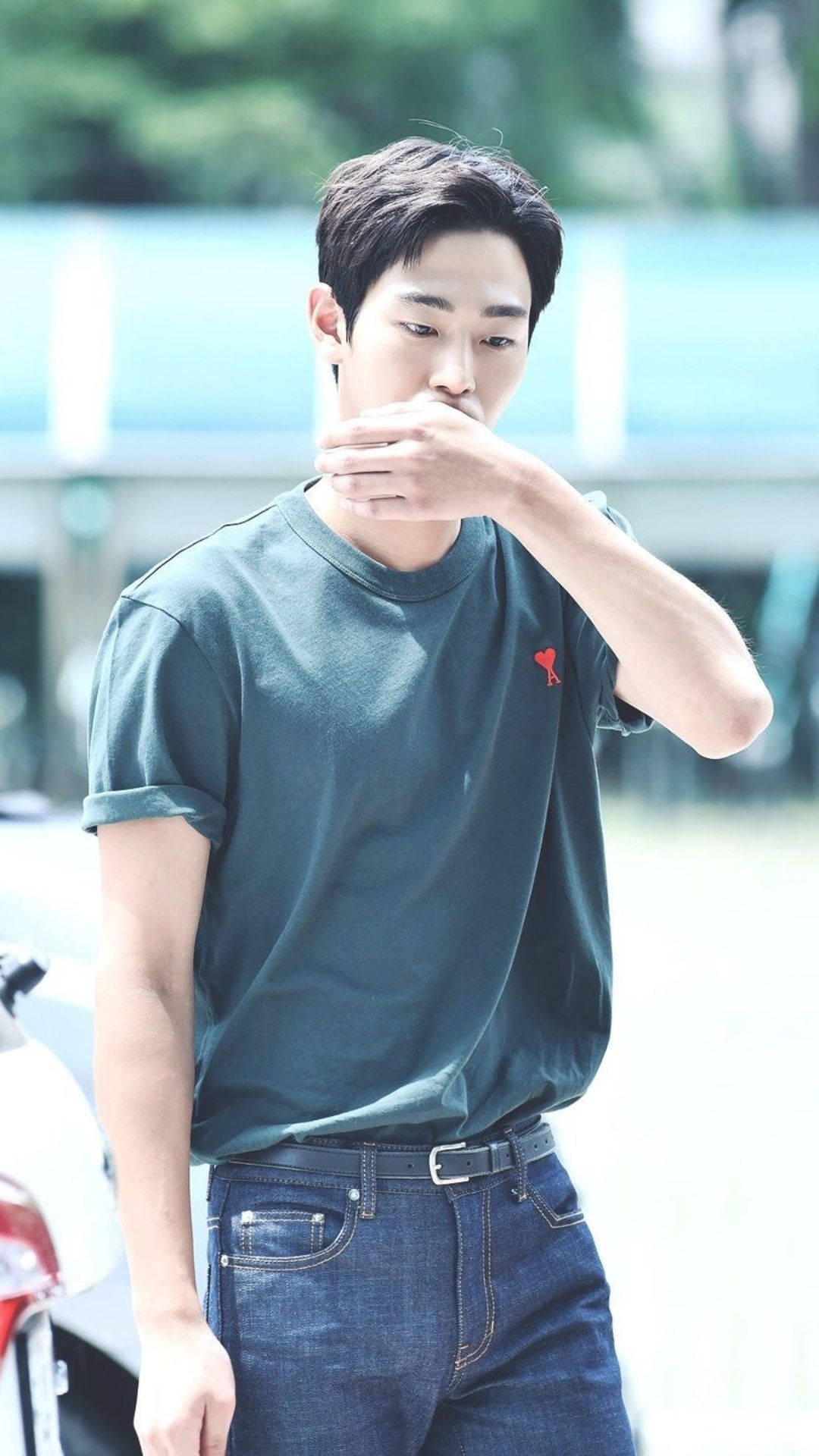 Ahn Hyo Seop 桌布 壁紙 — 一名身穿深綠色T恤和牛仔褲的年輕男子站在戶外，手靠近嘴邊，在明亮的日光下顯得若有所思。