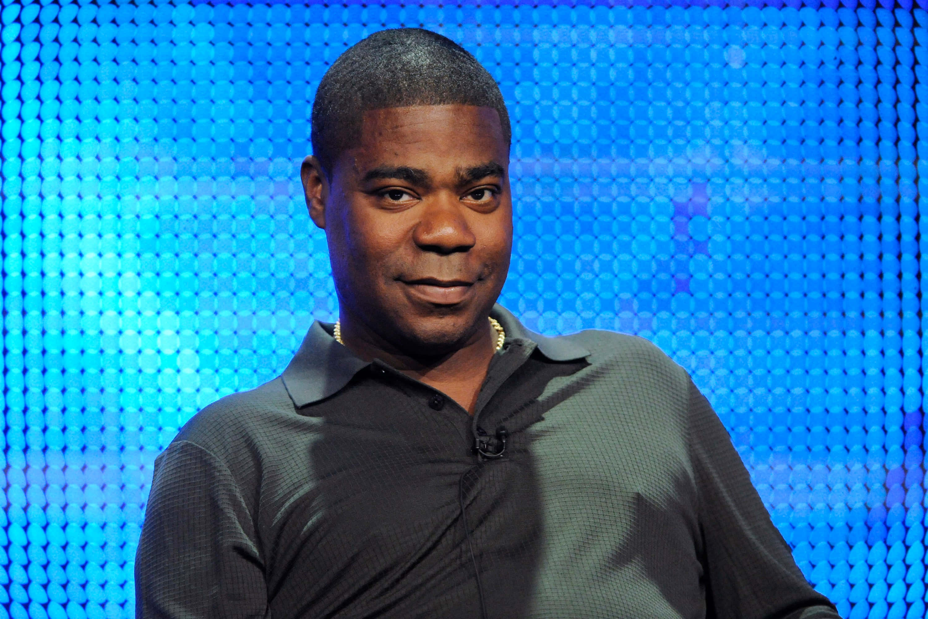 Tracy Morgan 桌布 壁紙 — 一名身穿深色Polo衫的男子在充滿活力的藍色像素化背景前微微微笑。