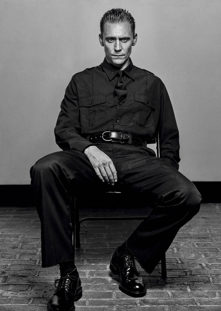 Tom 桌布 壁紙 — 一名身穿深色制服的男人莊嚴地坐在椅子上，背景是素牆和磚地板。