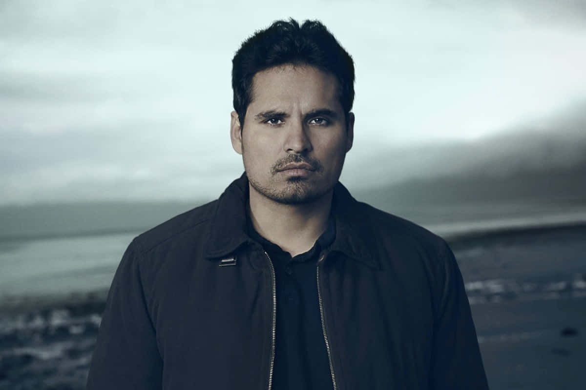 Michael Peña 桌布 壁紙 — 一名身穿深色外套的男子，在陰天之下，以霧氣瀰漫的海岸為背景，莊嚴地站立。
