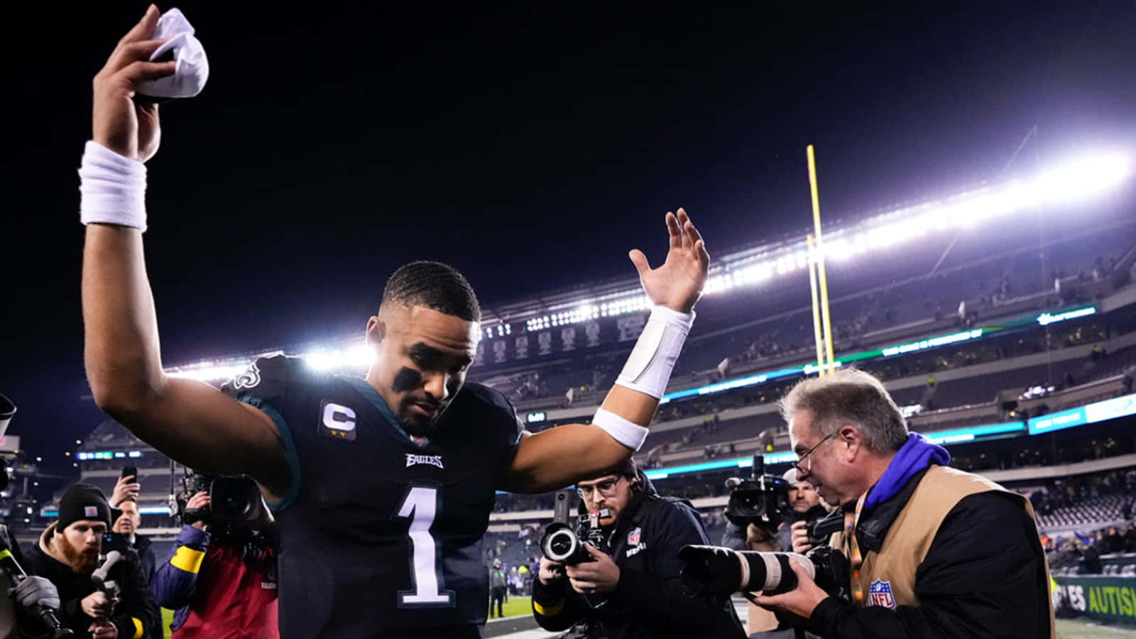 Football Player 桌布 壁紙 — 一名身穿深色球衣、背號1號的美式足球四分衛在夜間球場燈光下高舉雙臂慶祝勝利，攝影師捕捉了這一刻。