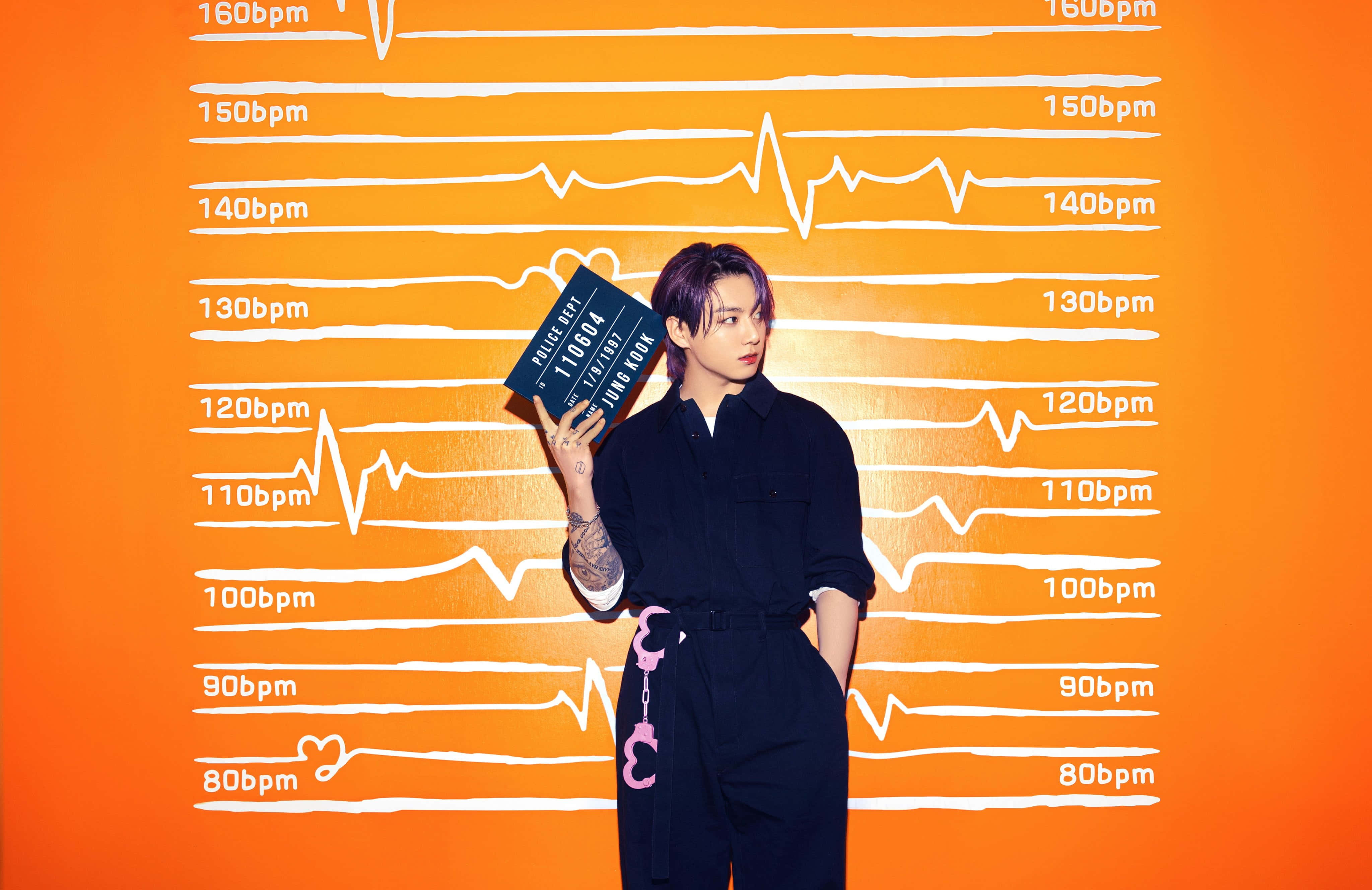 Jungkook 桌布 壁紙 — 一名身穿深色衣服的人，在帶有白色心跳線圖案的鮮橙色牆前舉著拍板。