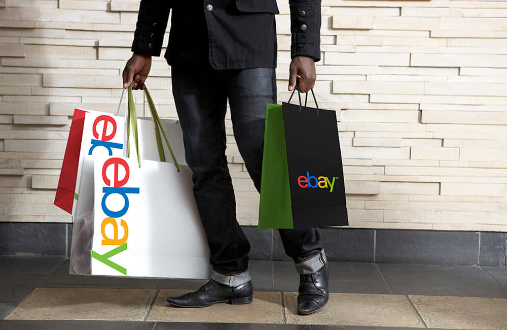 Shopping 桌布 壁紙 — 一名身穿深色衣服的人手持多個色彩繽紛的eBay購物袋，靠著現代紋理牆。