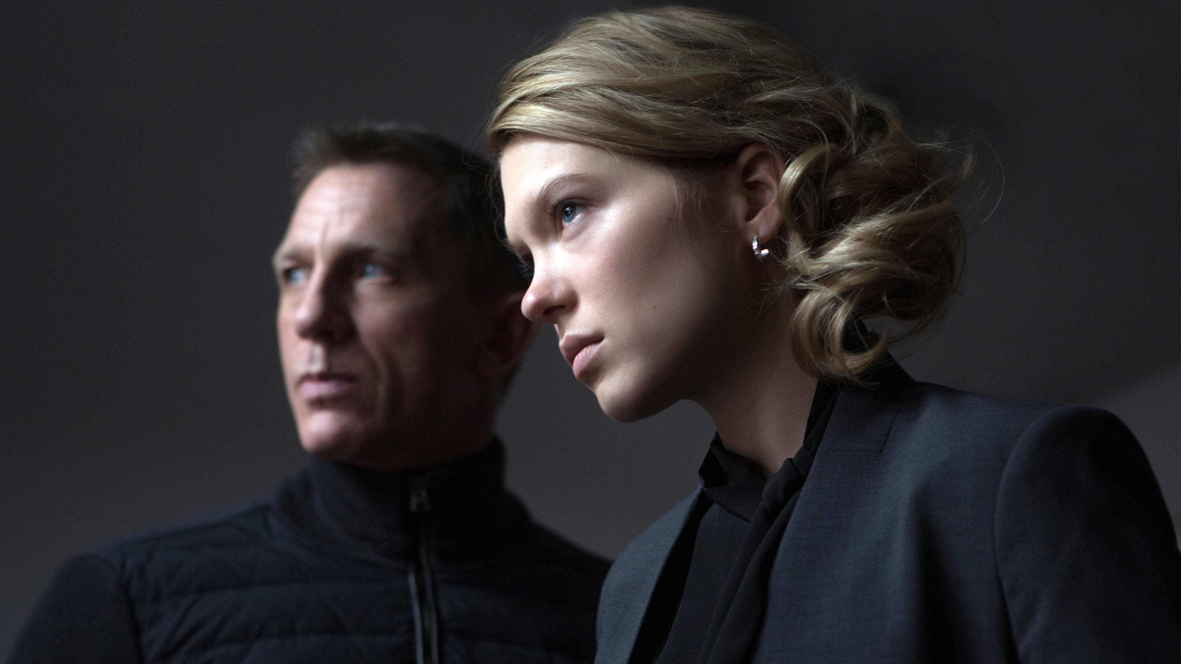 Daniel Craig 桌布 壁紙 — 一名身穿深色衣服的男女以陰影側面站在灰色背景前，嚴肅的表情傳達出緊張感。