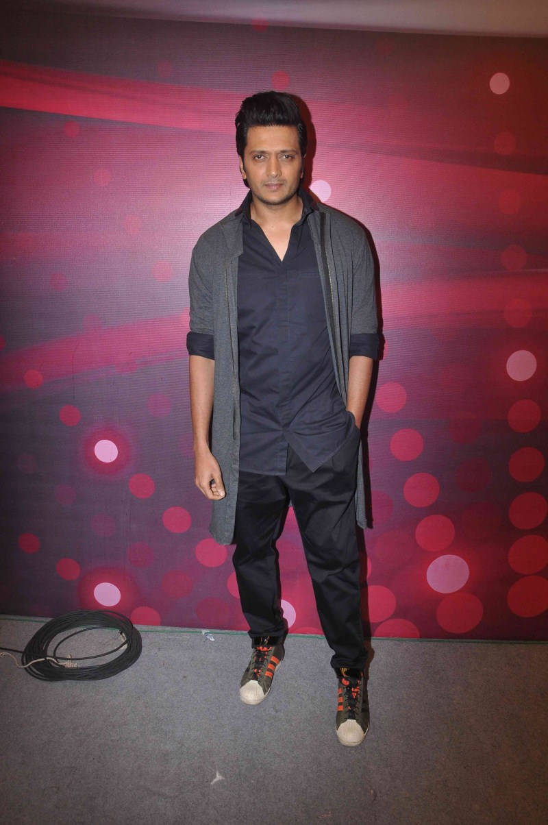 riteish deshmukh 桌布 壁紙 — 一名身穿深色衣服的男子自信地站在充滿活力的紅色和紫色散景燈光背景前。