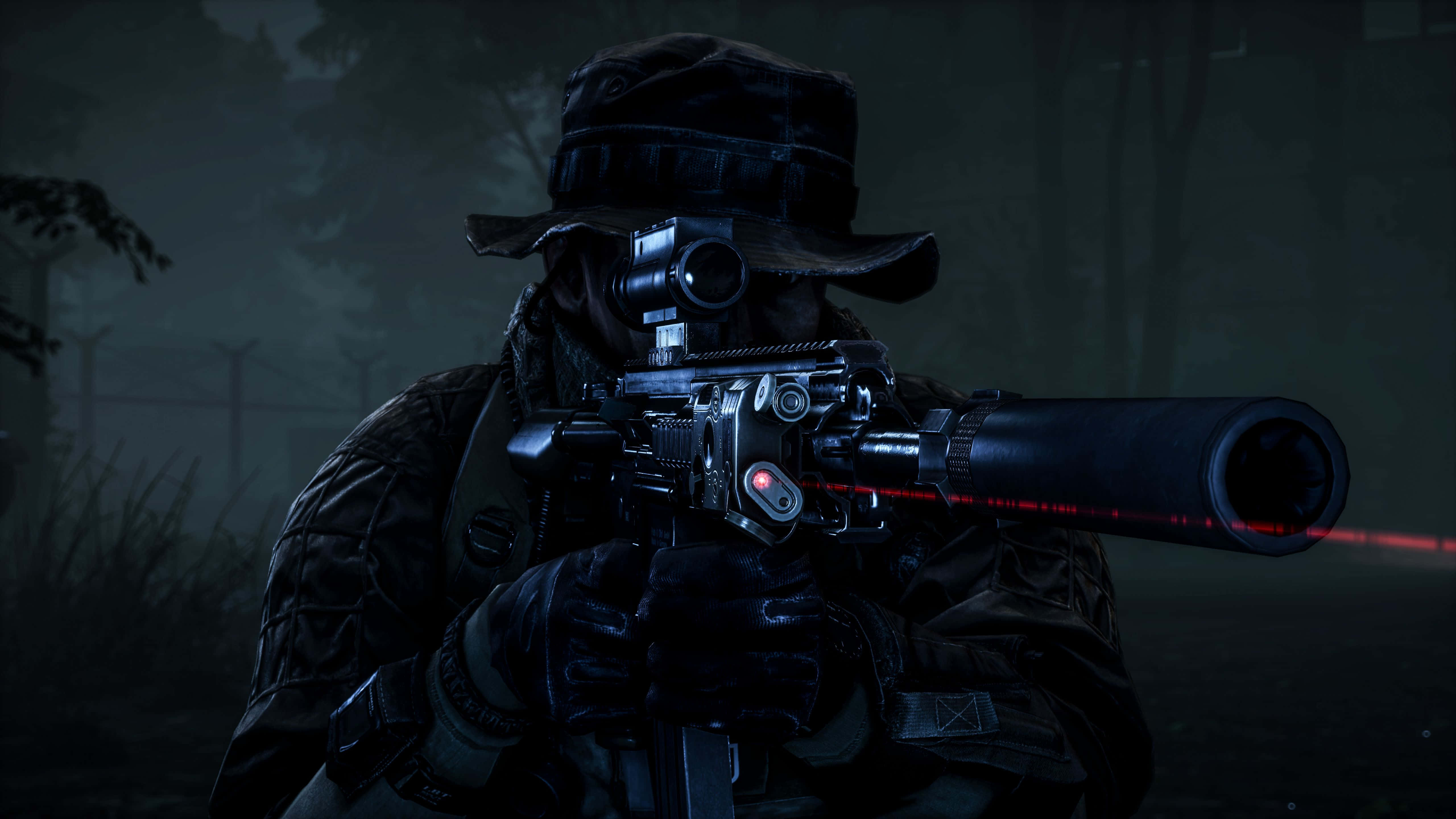 4K Battlefield 桌布 壁紙 — 一名身穿深色裝備的士兵在夜間透過霧氣瀰漫的森林用帶有紅色雷射瞄準器的步槍瞄準。