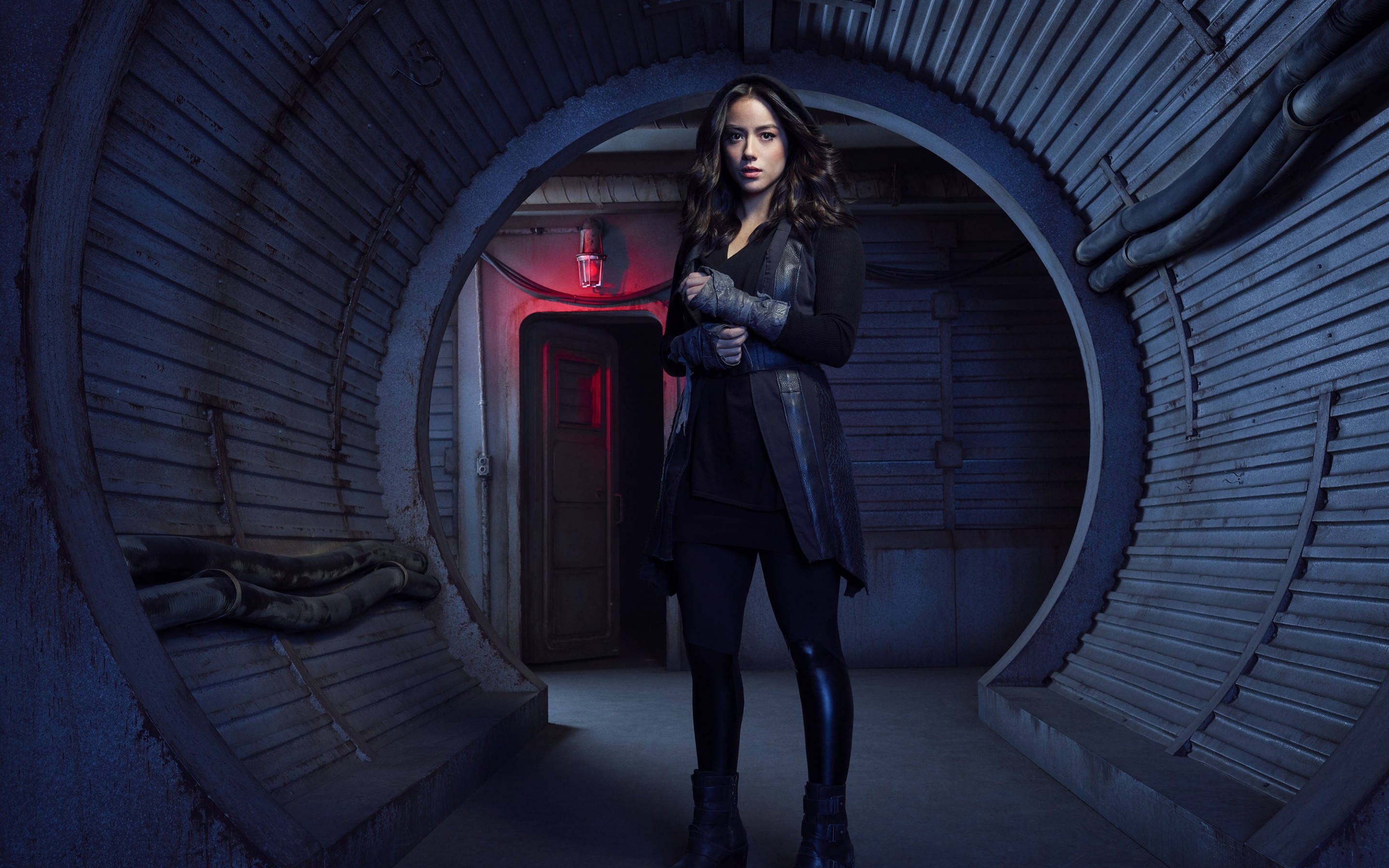 agents of shield 桌布 壁紙 — 一名身穿深色裝備的女性，在昏暗的工業隧道中挑釁地站立，紅色應急燈投射出詭異的陰影。