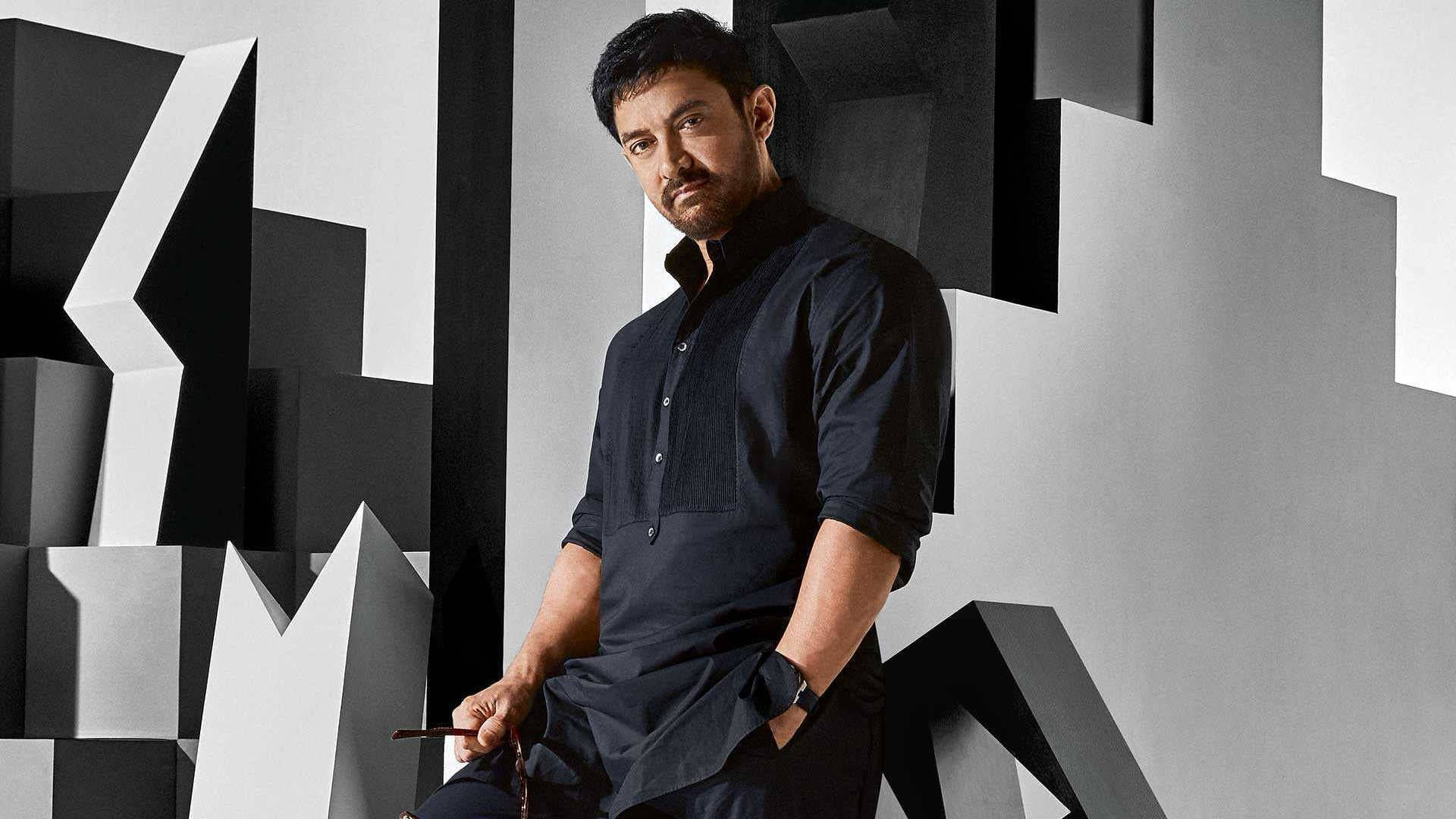 Aamir Khan 桌布 壁紙 — 一名身穿深色襯衫的男子，在一個帶有尖銳角形的大膽黑白幾何牆壁前自信地擺姿勢。