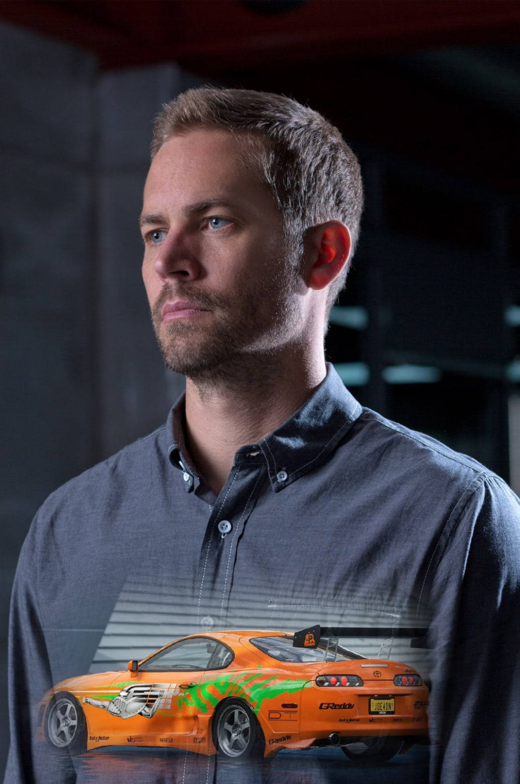 Paul Walker 桌布 壁紙 — 一名身穿深色襯衫的男子若有所思地凝視著，一輛帶有綠色火焰的橙色賽車半透明地疊加在他的胸前。