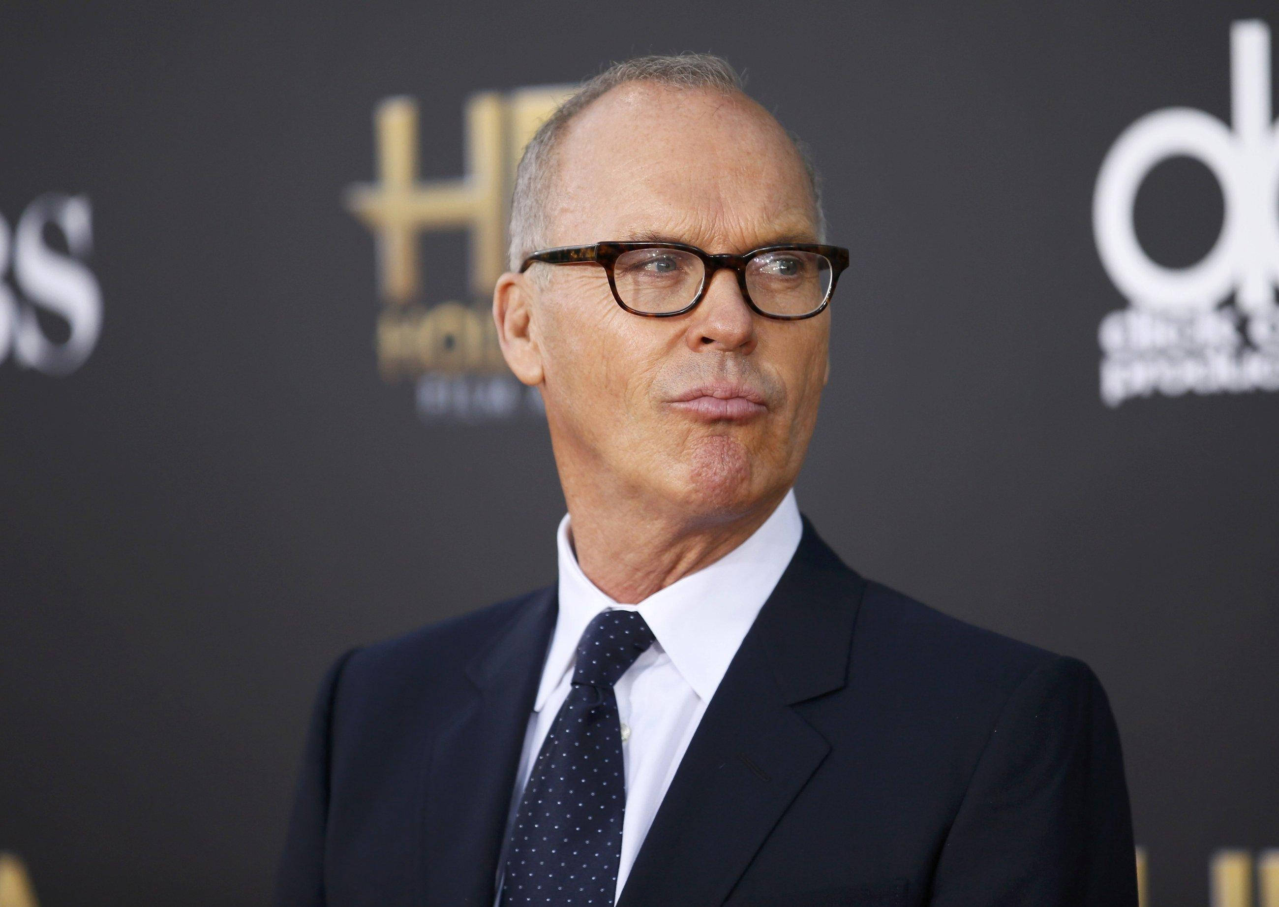 Celebrity 桌布 壁紙 — 一名身穿深色西裝、戴眼鏡的男子在品牌背景前，於正式活動中擺出嚴肅的表情。
