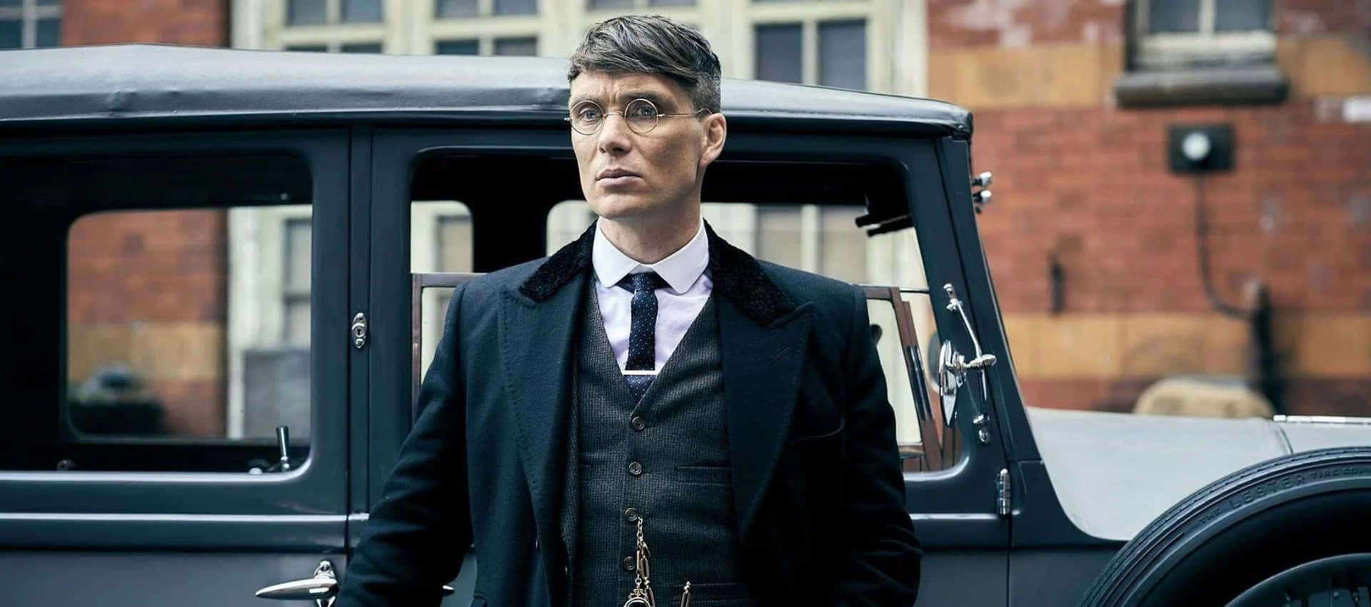 穿西裝戴眼鏡的男子站在城市環境中的復古汽車旁 — Peaky Blinders 壁紙