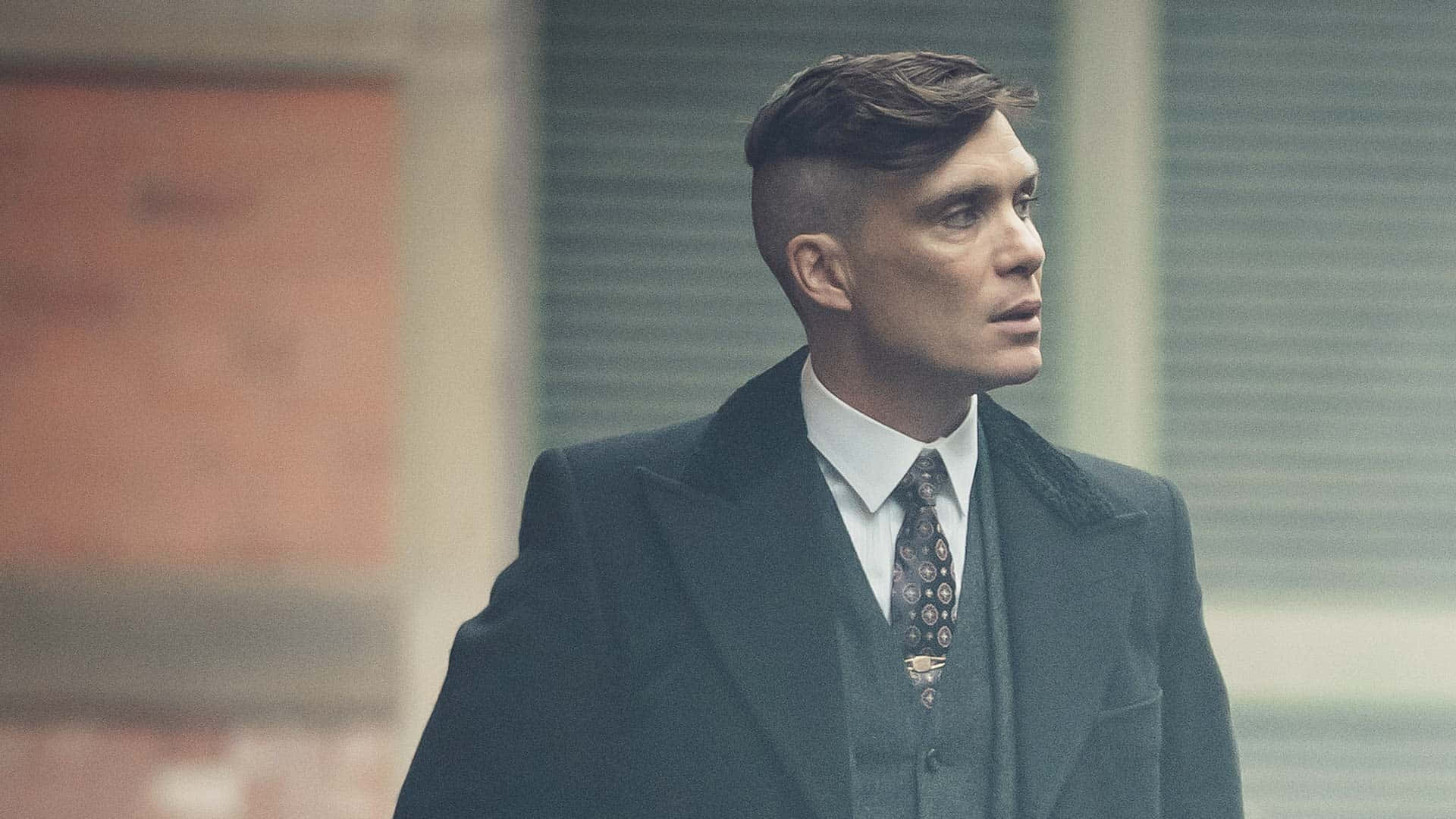 身穿深色西裝及圖案領帶的男子站在霧氣瀰漫的都市街道上。 — Peaky Blinders 壁紙