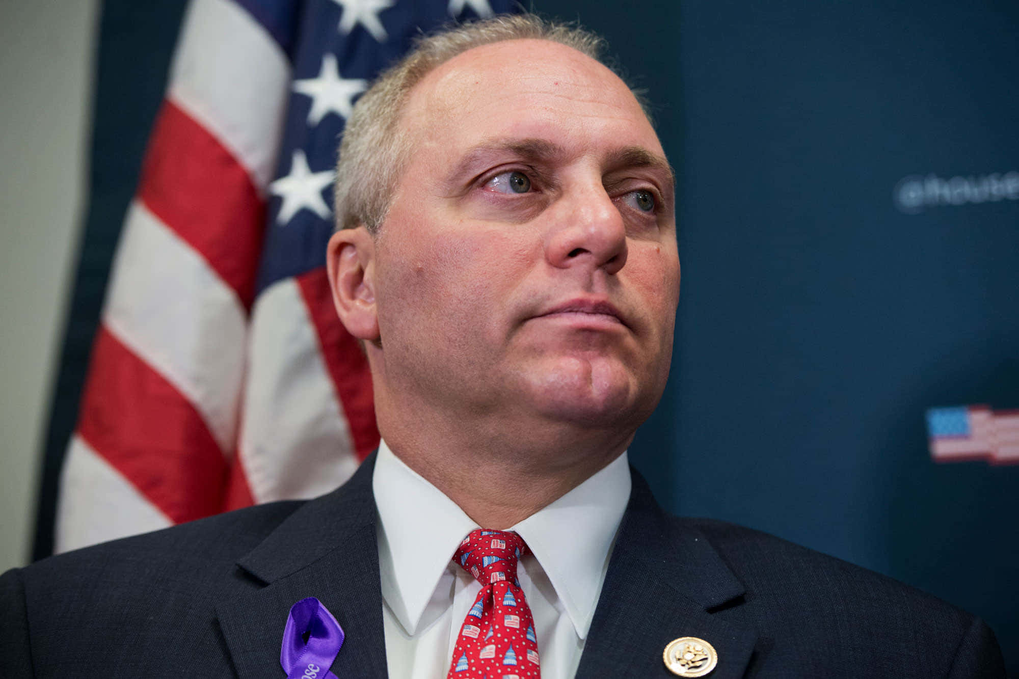 Celebrity 桌布 壁紙 — 一名身穿深色西裝和紅色領帶的男子，在美國國旗背景下嚴肅地向上仰望。