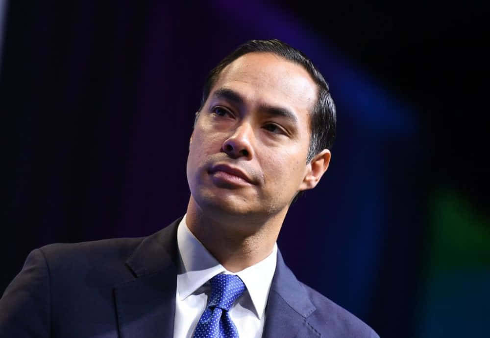 Celebrity 桌布 壁紙 — 一名身穿深色西裝和藍色領帶的男子，在模糊的深色背景下，帶著沉思的表情向上仰望。
