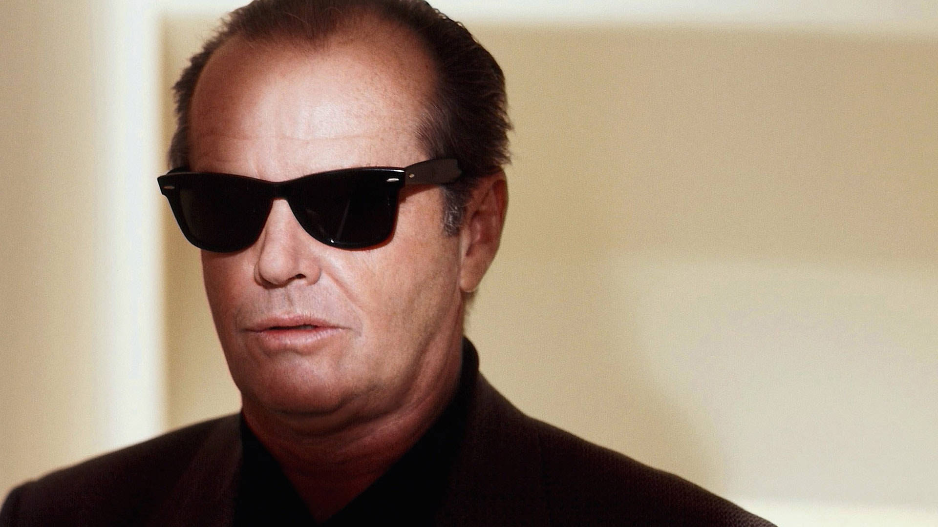 Sunglasses 桌布 壁紙 — 一名身穿深色西裝和黑色太陽眼鏡的男子，在純米色背景下，神情嚴肅地凝視著。