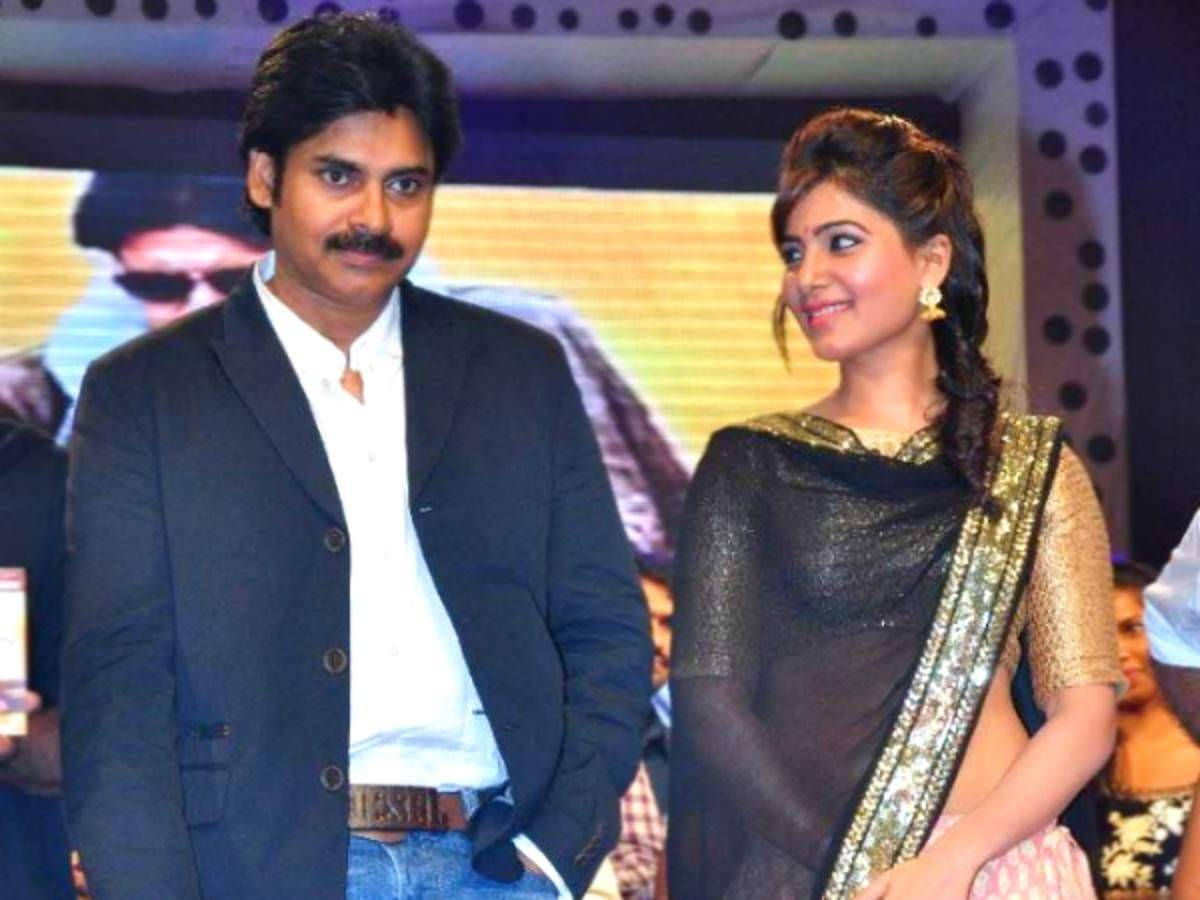 Pawan Kalyan 桌布 壁紙 — 一名身穿深色西裝外套和牛仔褲的男子，站在一位身穿金色滾邊黑色紗麗的女子身旁，身處燈光明亮的活動場合。